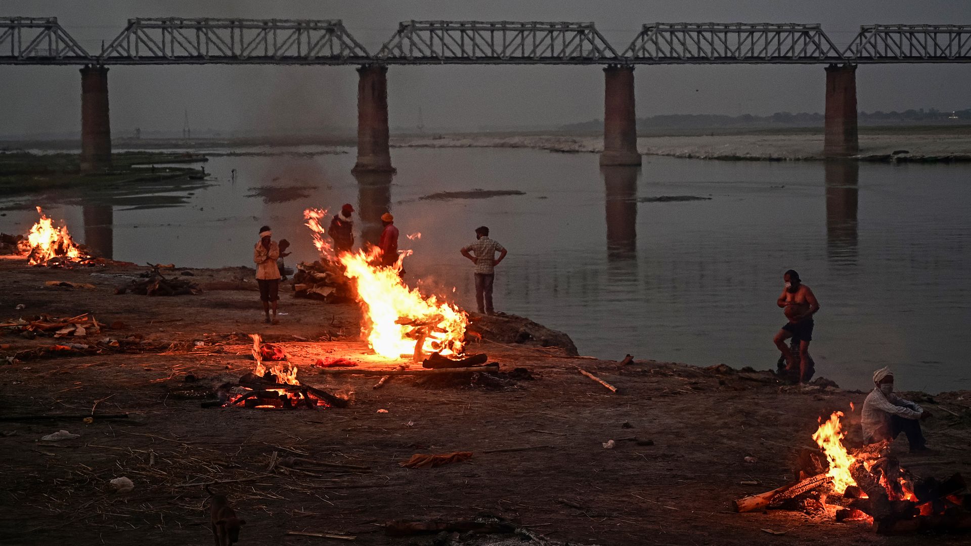 People watch unclaimed bodies burn on funeral pyres at a mass crematorium site on the banks of the Ganges river on May 05, 2021 in Allahabad, India.