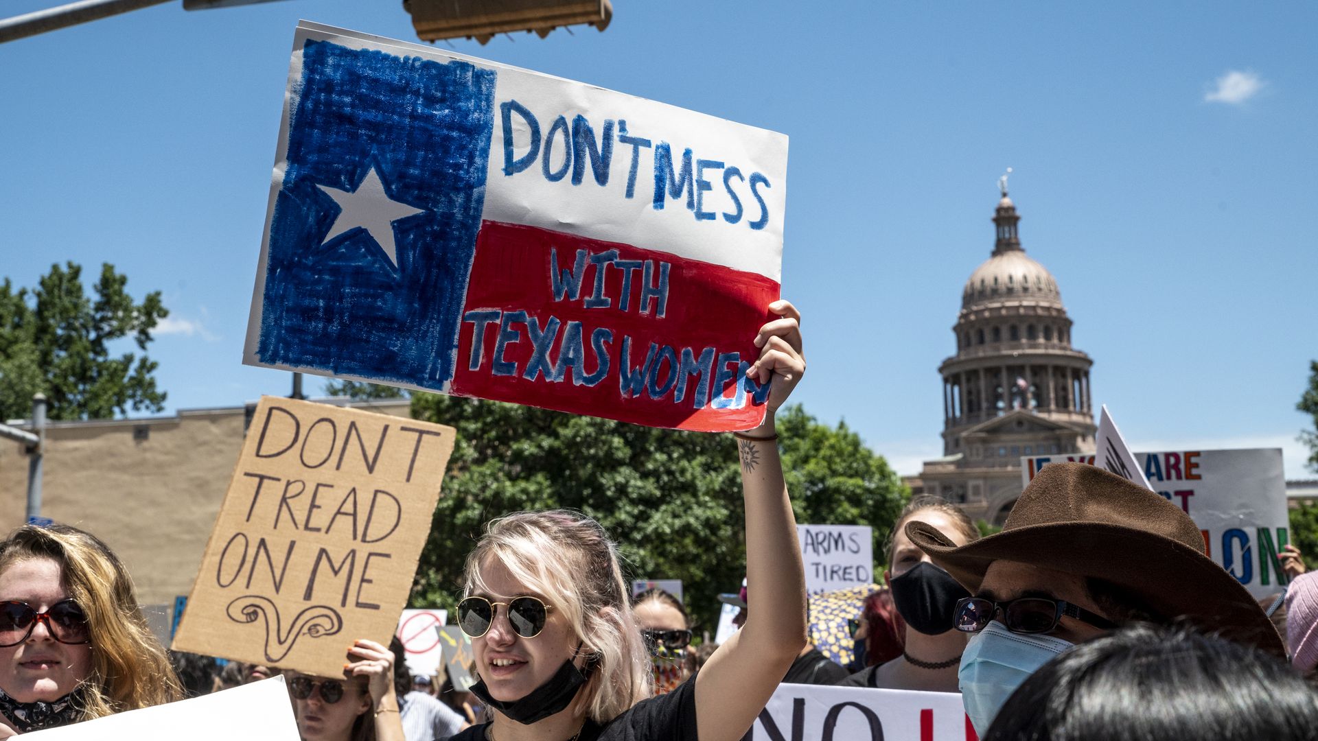 Photo of a person holding a sign that's in the design of a Texas flag and says "Don't mess with Texas women"