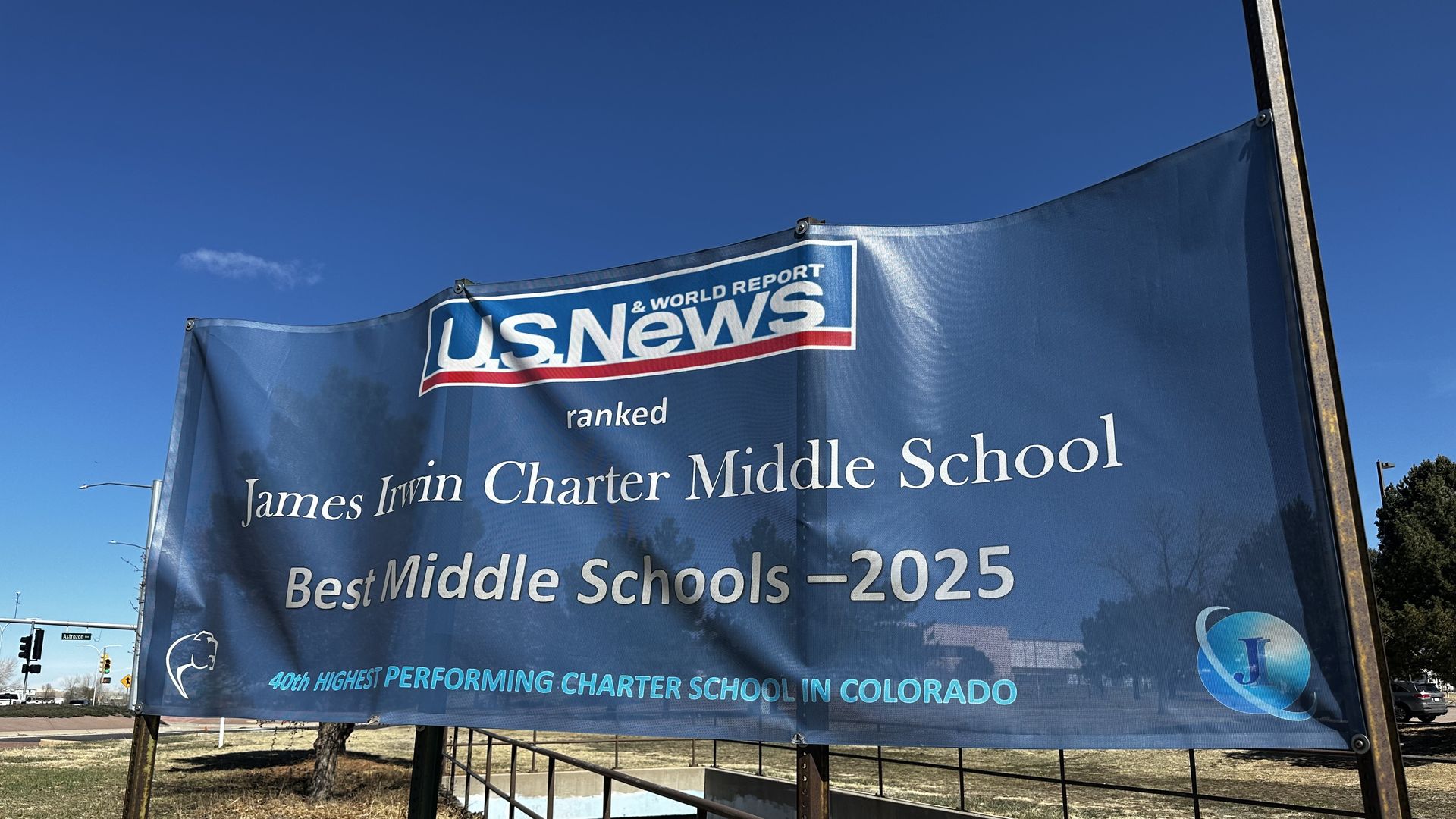 Blue banner on metal posts with the "U.S. News" logo reads "James Irwin Charter Middle School" and "Best Middle Schools - 2025" against a clear blue sky.
