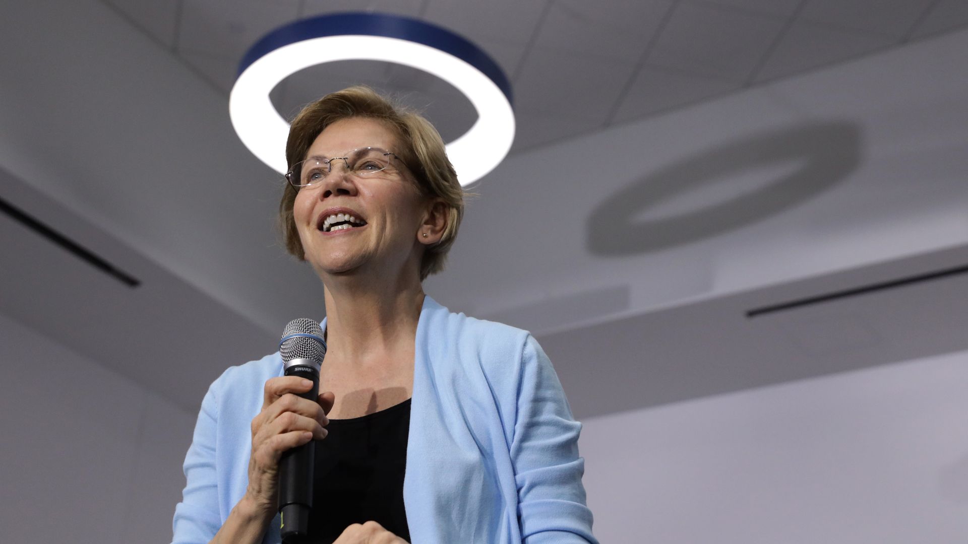 Elizabeth Warren stands under a light fixture that looks like a halo 