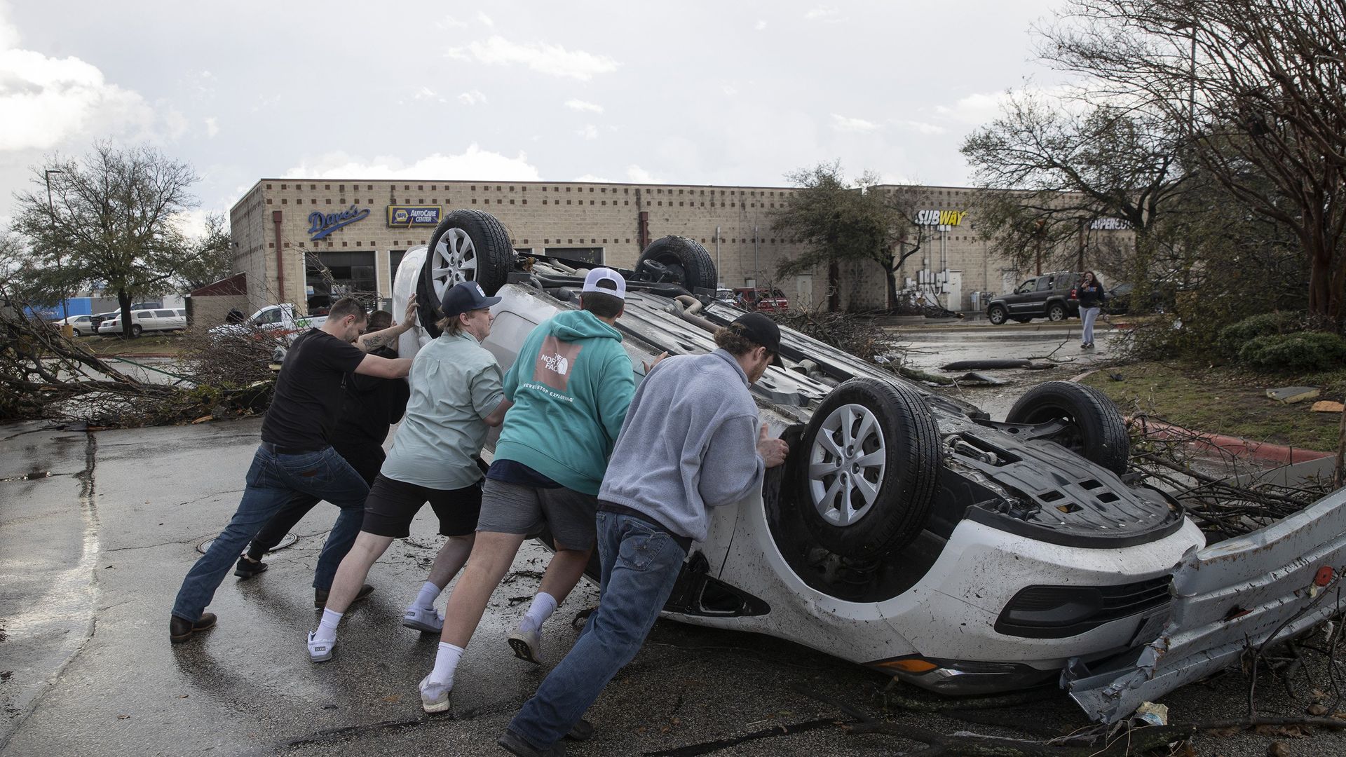 People try flipping a car overturned by a tornado.