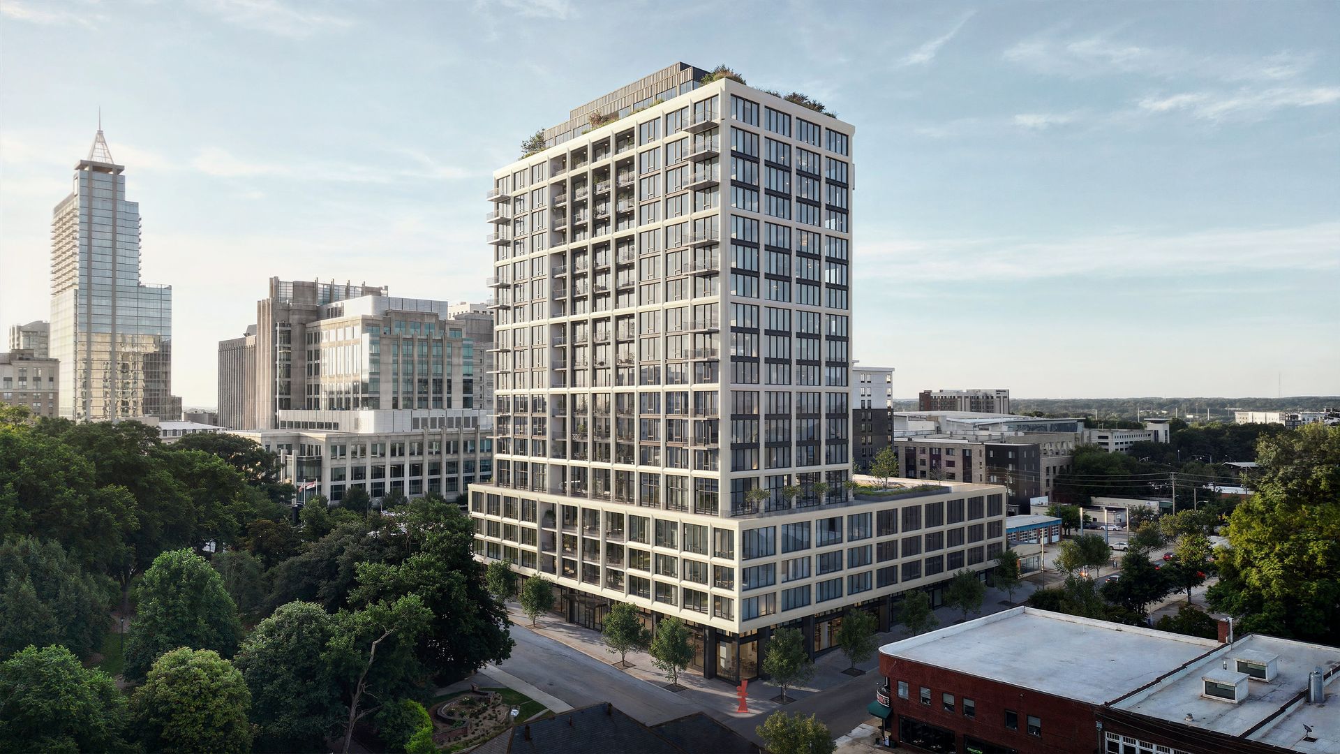 Modern multi-story building with glass windows and balconies, surrounded by cityscape with other buildings and green trees under a clear sky.