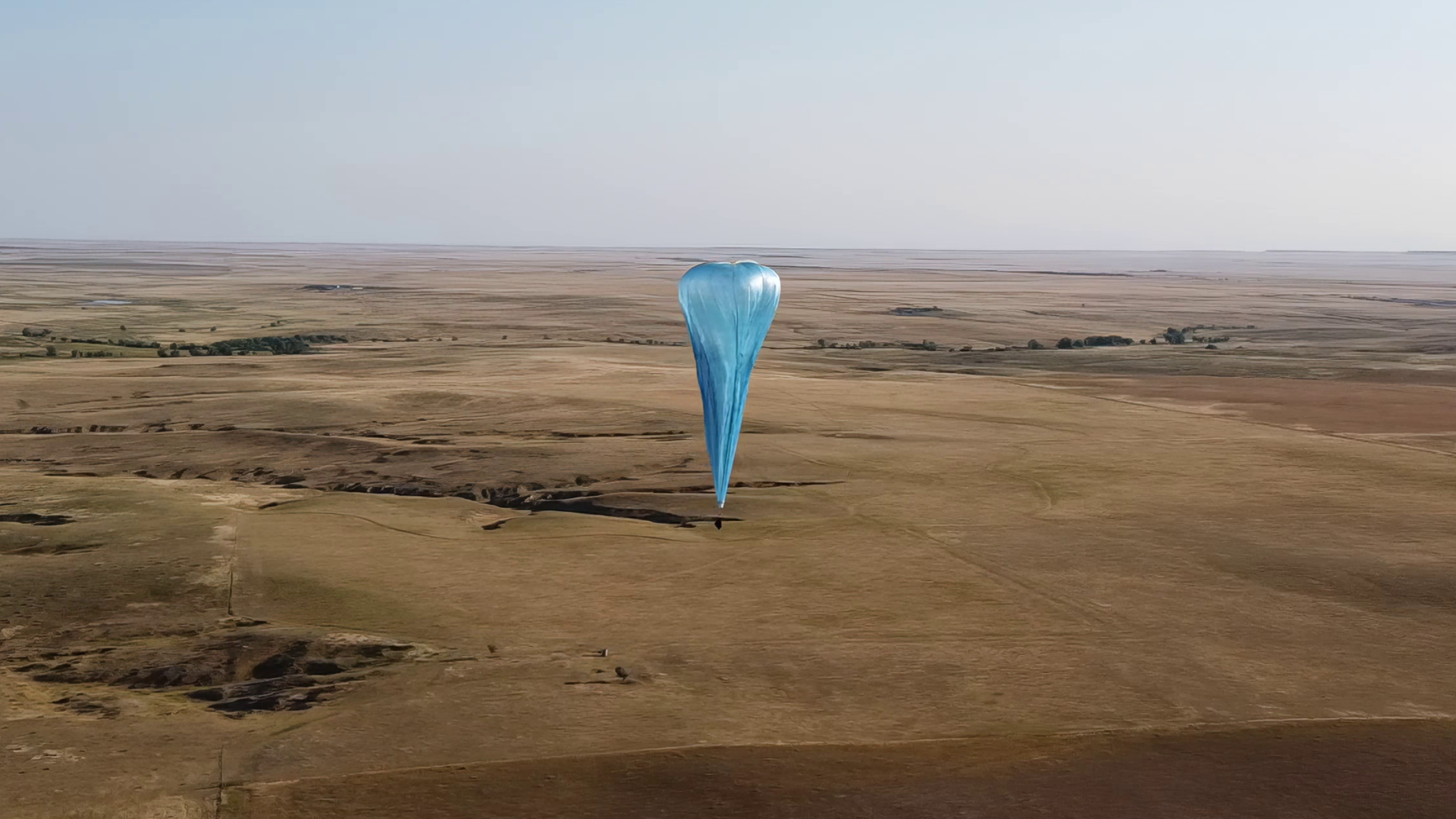 A blue balloon flies over mostly empty land on a clear day. 