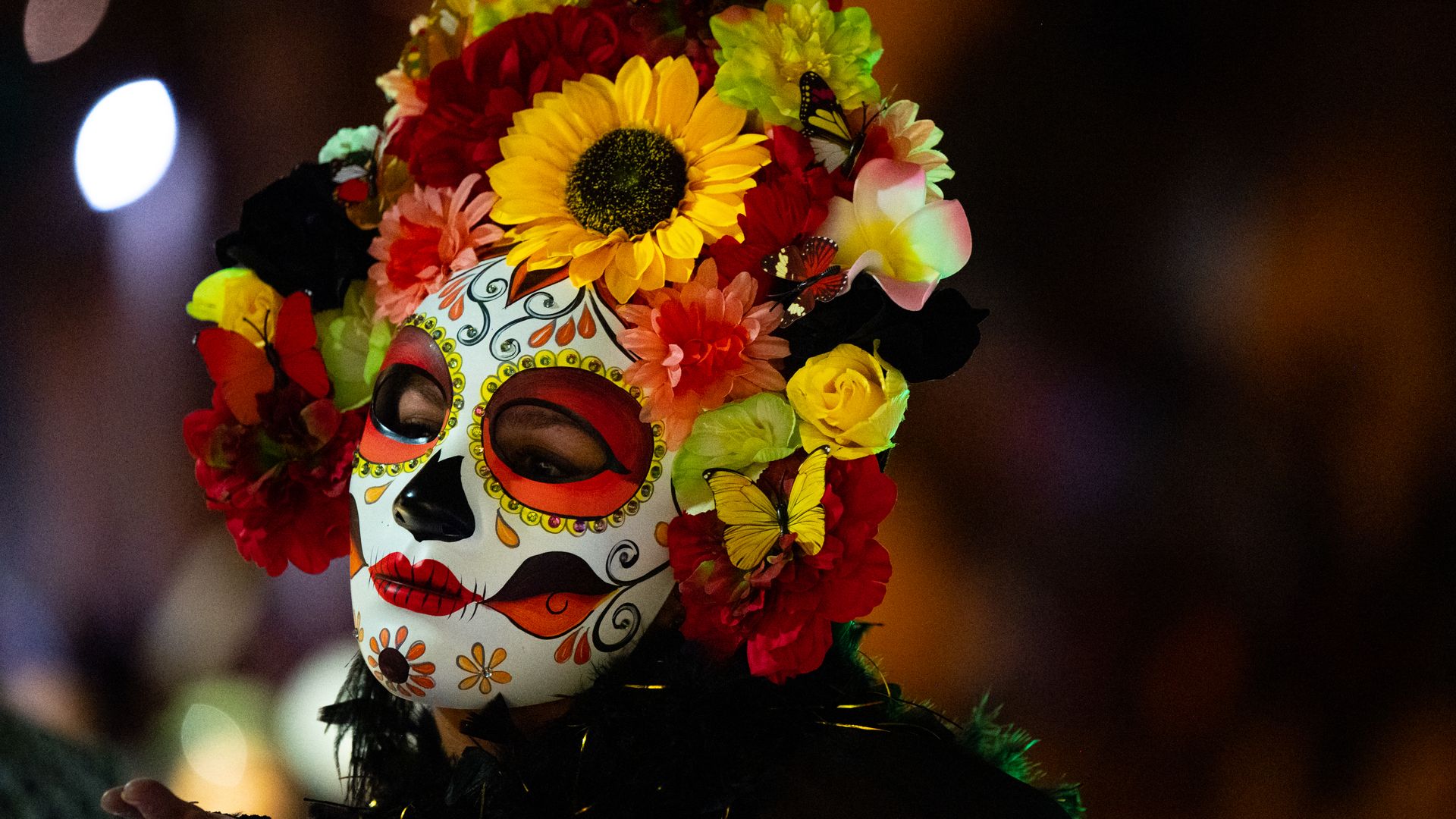 A woman wearing a mask depicting a traditional calavera face with flowers on her head.
