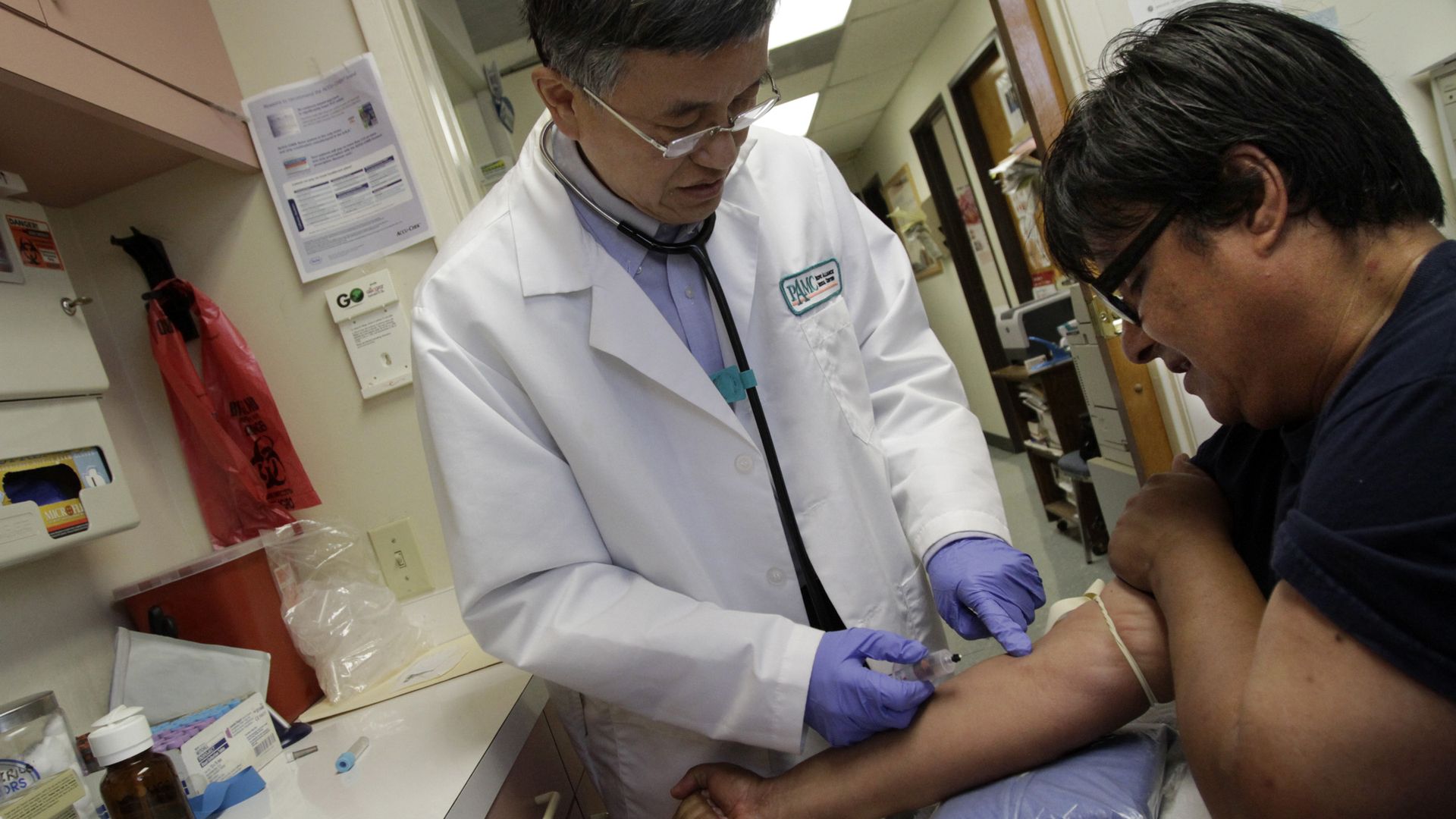 A doctor draws blood from a patient, whose arm is resting on a table.