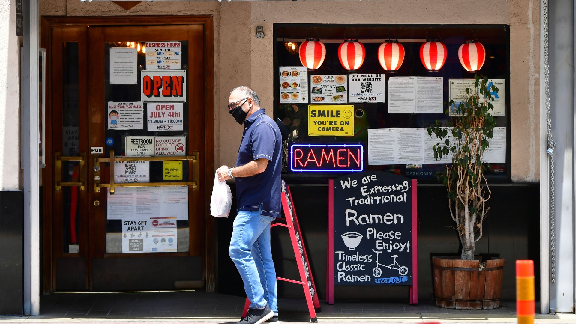 A man holding a plastic bag walks past a restaurant door