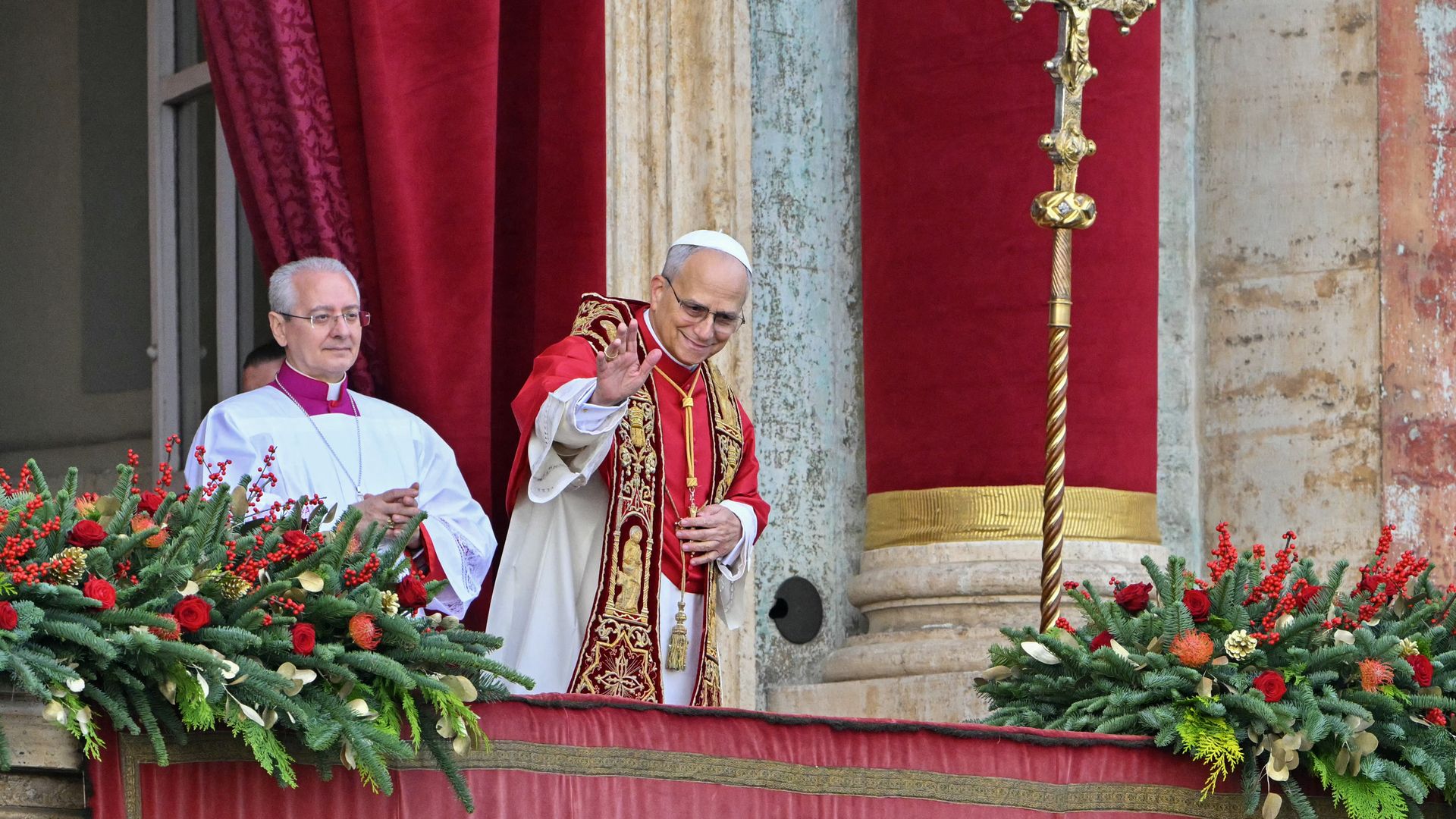 Pope Leo XIV, wearing red Christmas vestments, waves from the central balcony of St. Peter’s Basilica overlooking St. Peter’s Square at the Vatican.