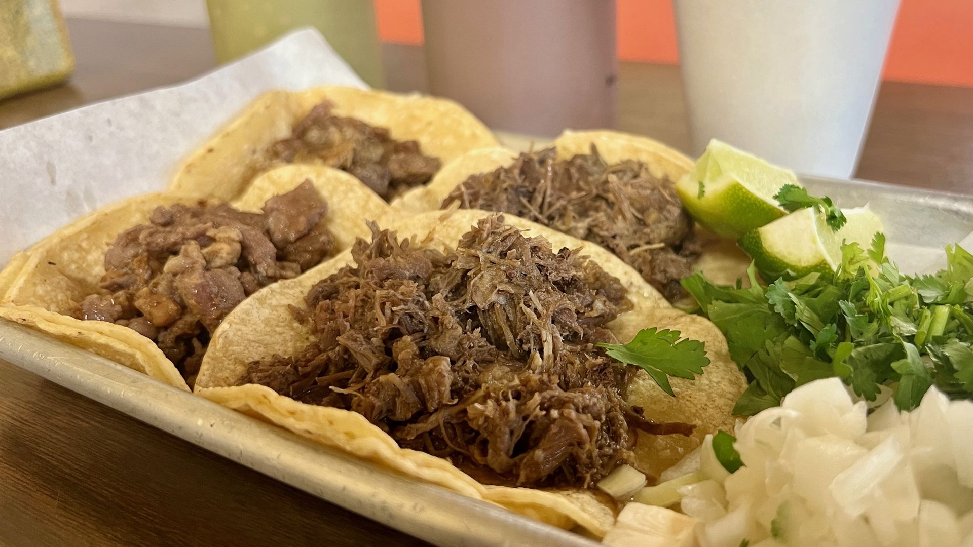 Four beef tacos with cilantro and onions on the side
