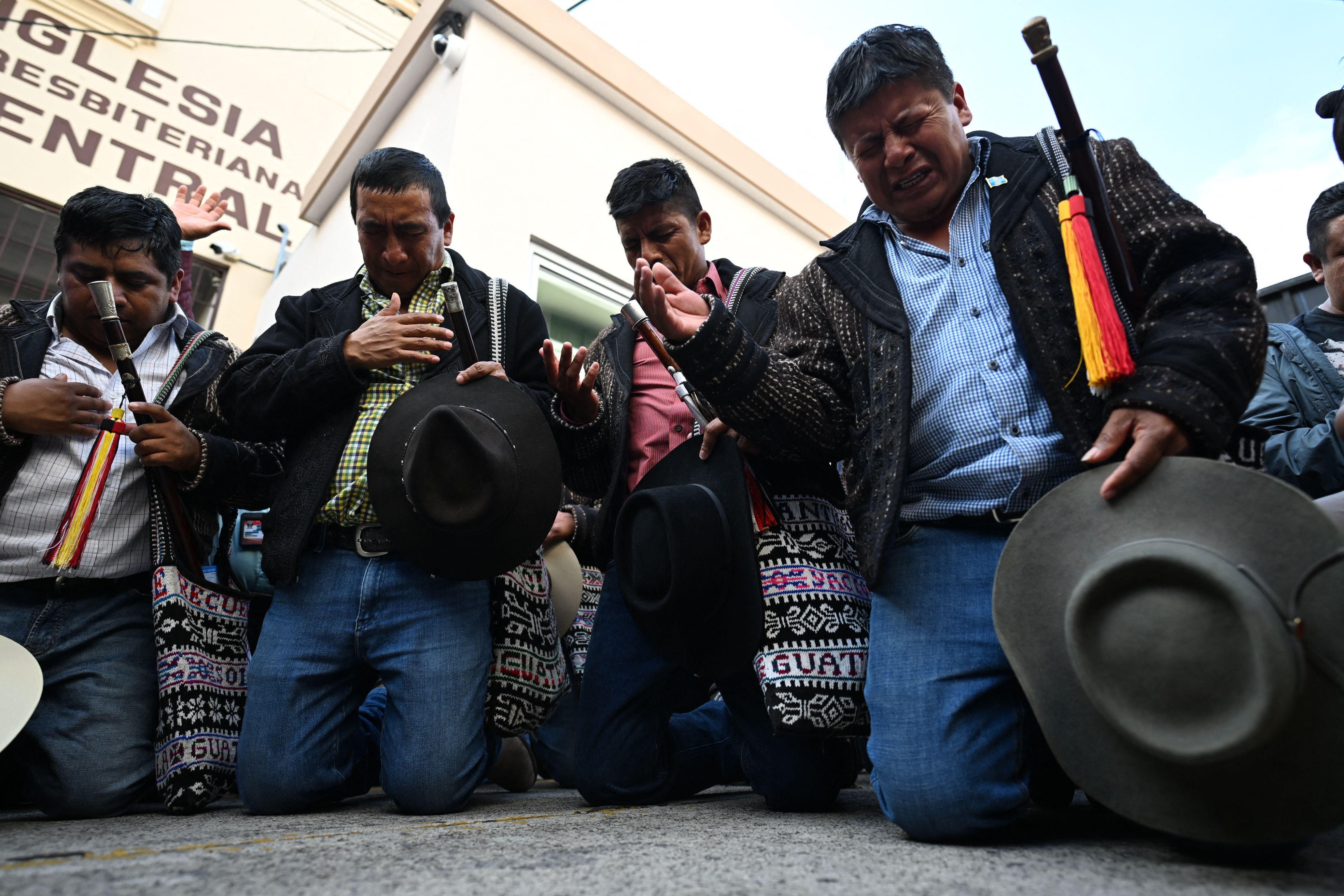 For men kneel on the ground, holding their hats and praying during a protest against the attorney general in Guatemala. 
