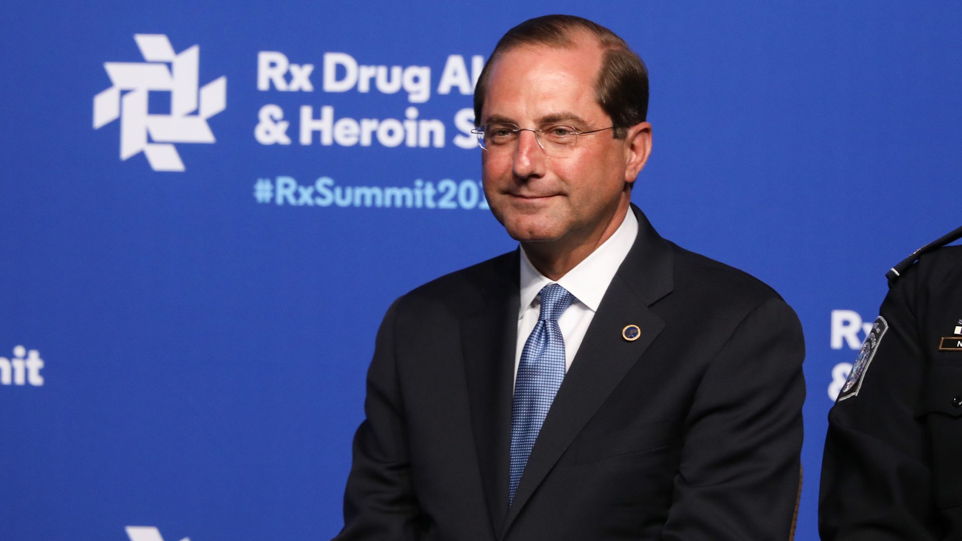 In this image, Alex M. Azar II stands and smiles faintly.