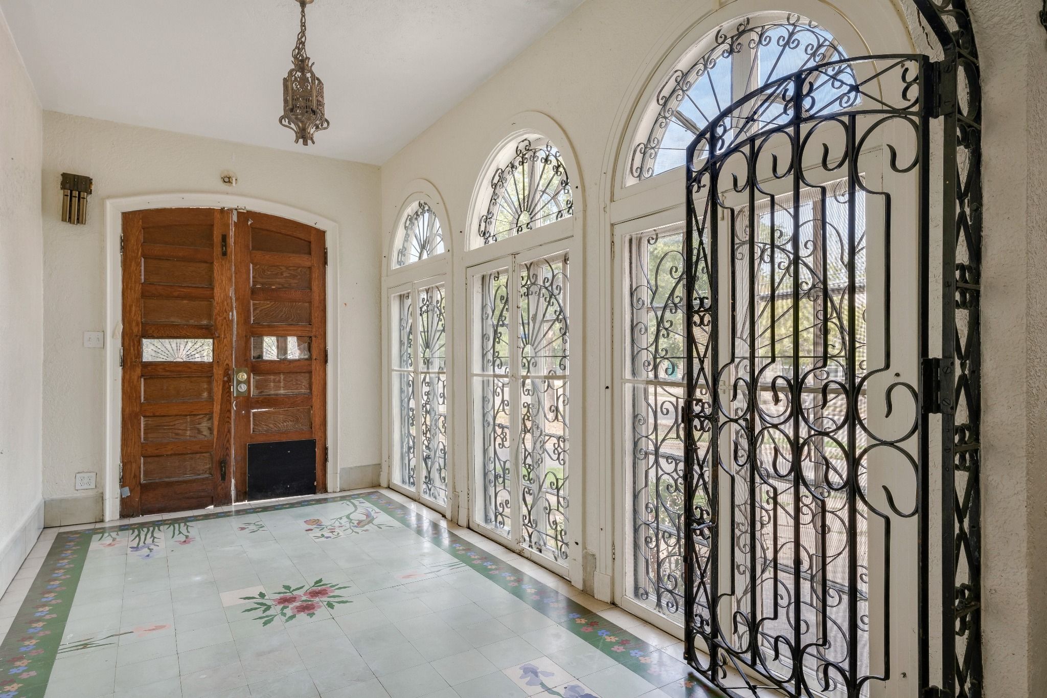 An entryway to a historic home with tall windows and iron accents, and a floral patterned floor.
