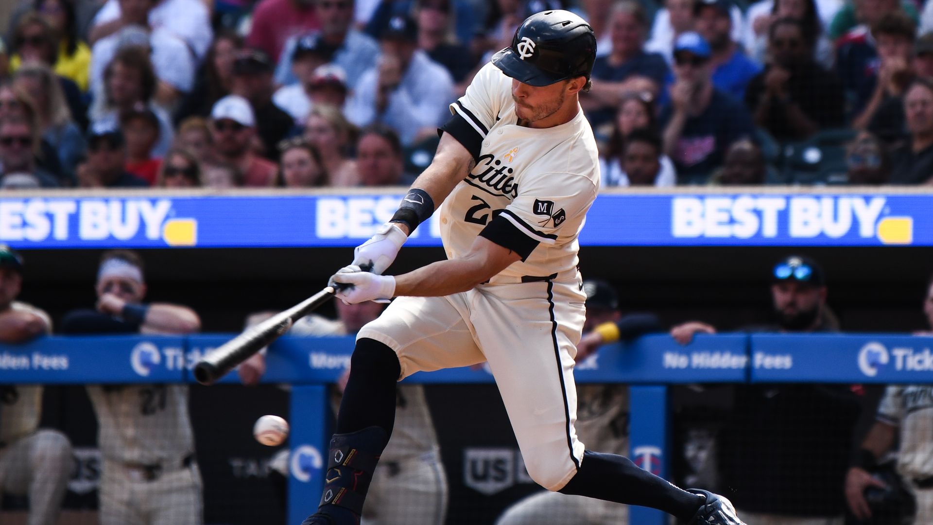 A baseball player in an off-white jersey with a dark blue helmet featuring a 'TC' logo swings at a pitch