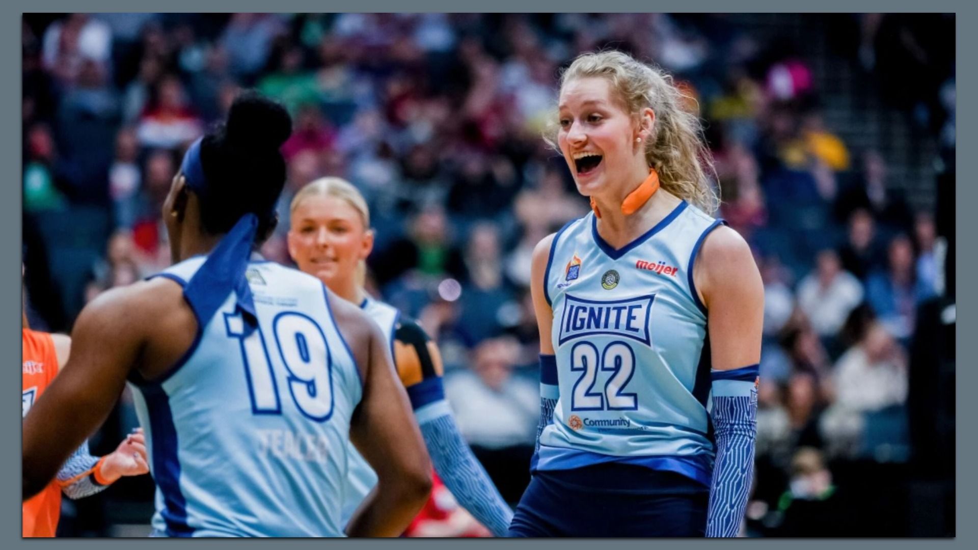 Three female basketball players in light blue Ignite jerseys with numbers 19 and 22, one smiling excitedly during a game with a blurred crowd in the background.