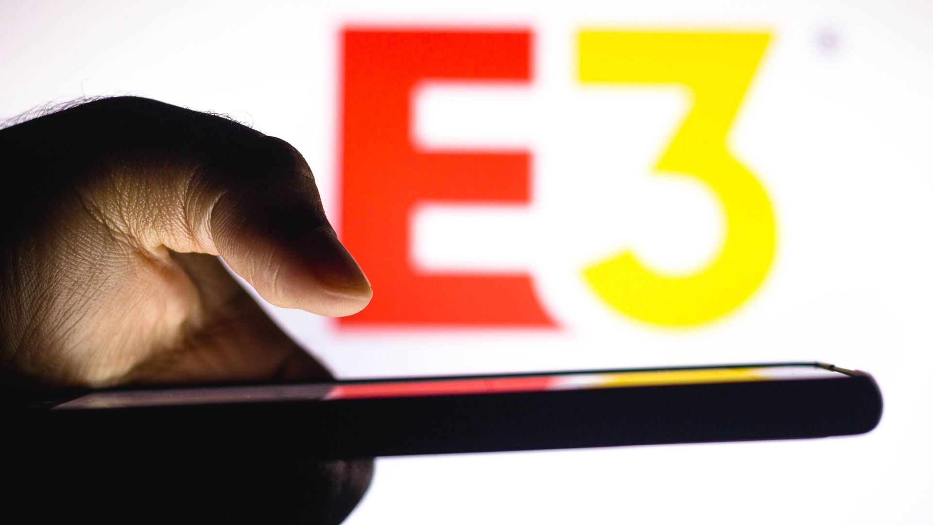 In this photo illustration, a hand of a person holds a smartphone with an Electronic Entertainment Expo (E3) logo displayed in the background.