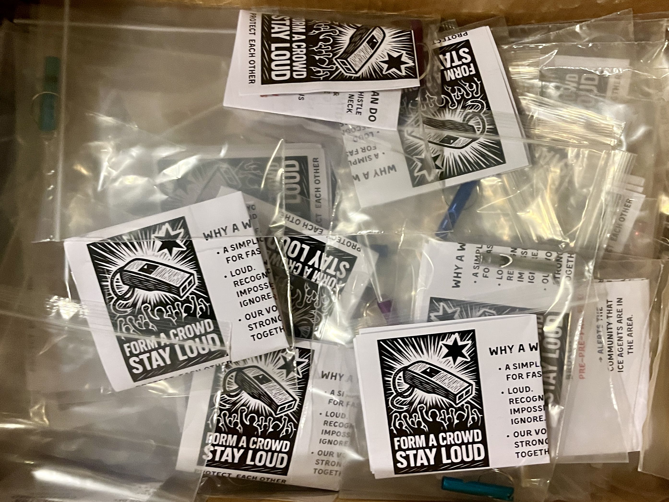 Several small plastic bags containing blue and purple whistles and black-and-white cards with a whistle image and text that says "Form a crowd, stay loud."