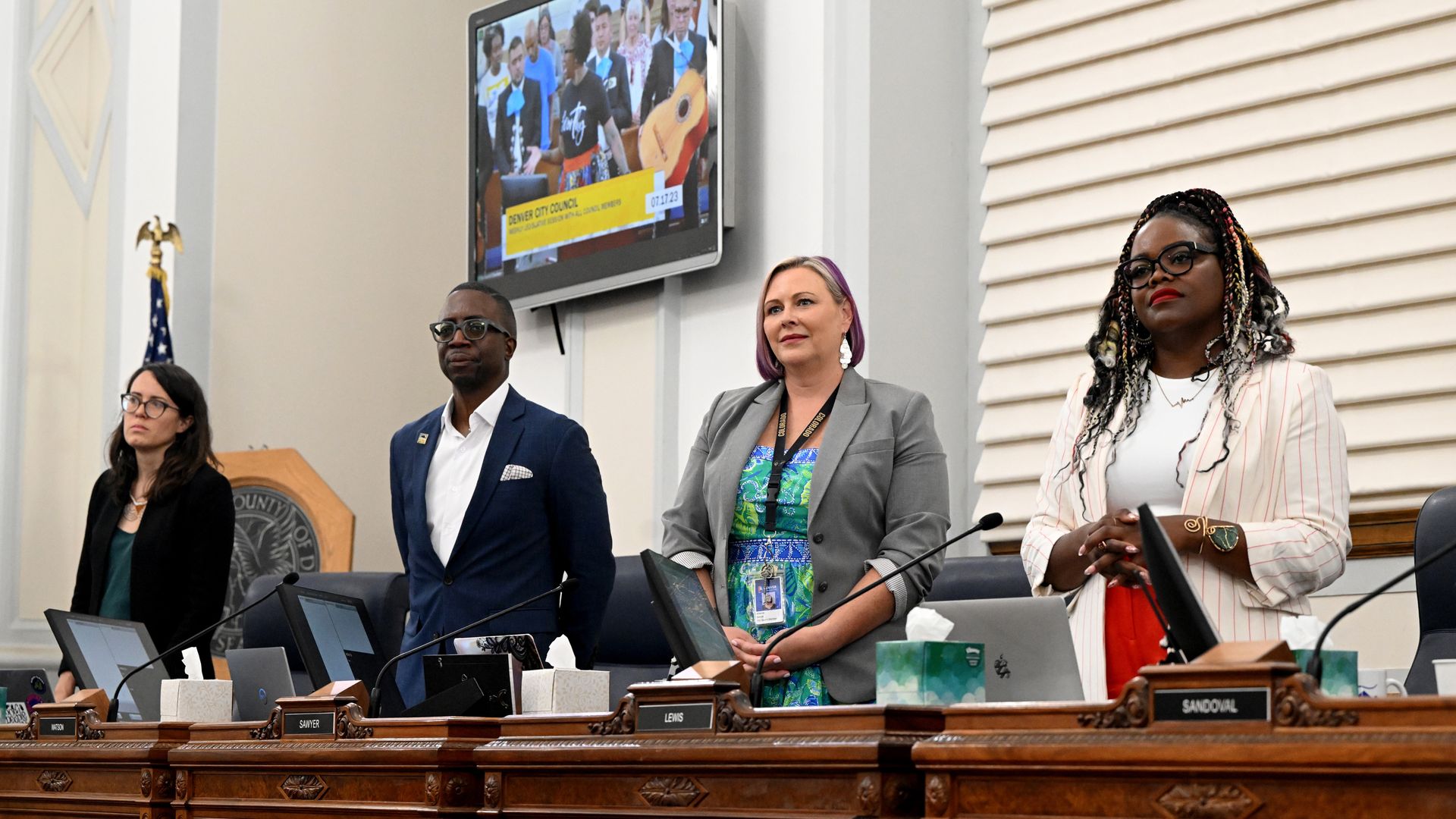 Four people in professional attire stand while looking ahead inside a brightly lit room. 