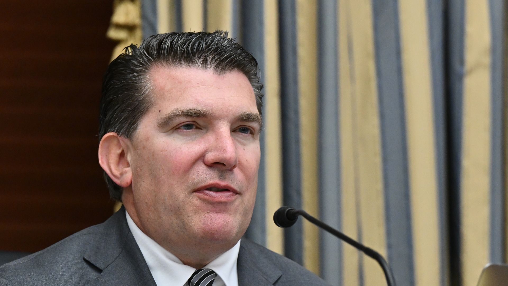 A person in a suit and tie speaks in front of a microphone