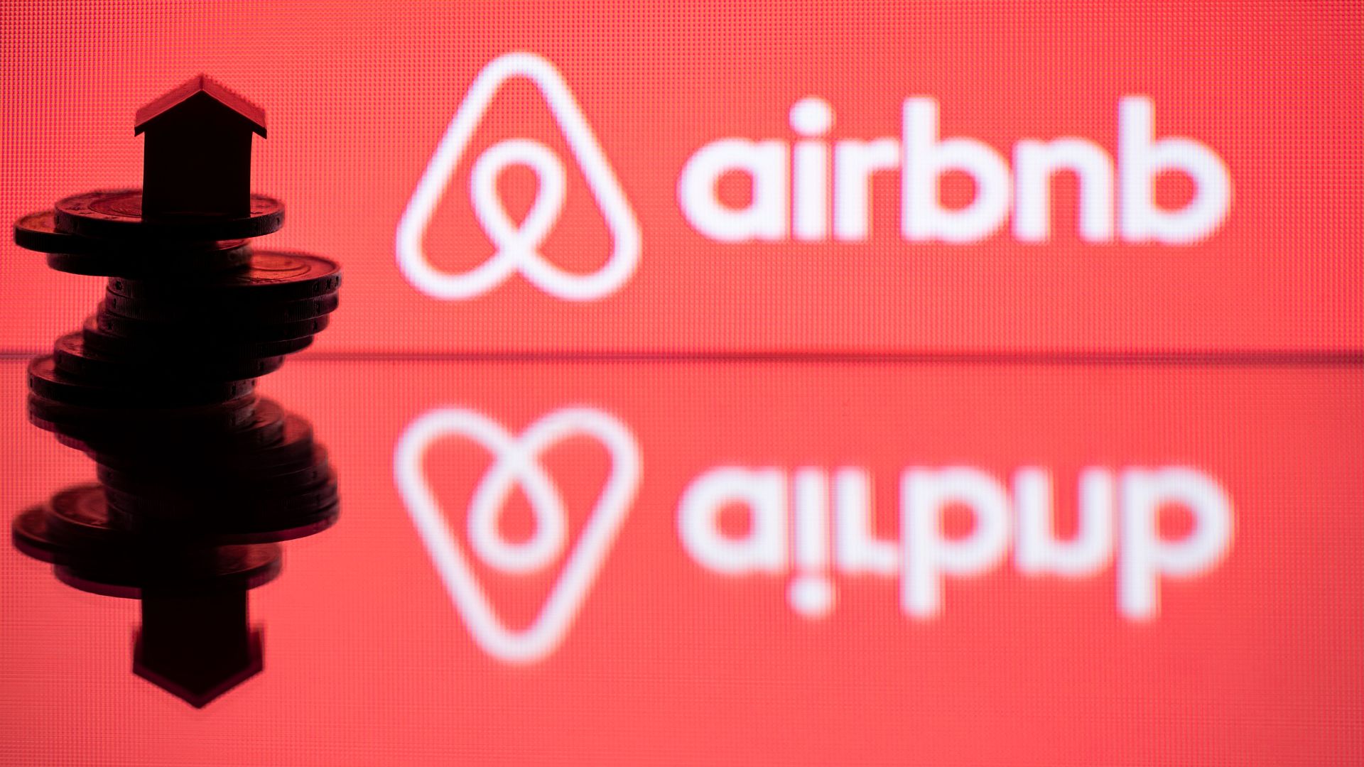 A toy house on coins next to the logo of housing website Airbnb.