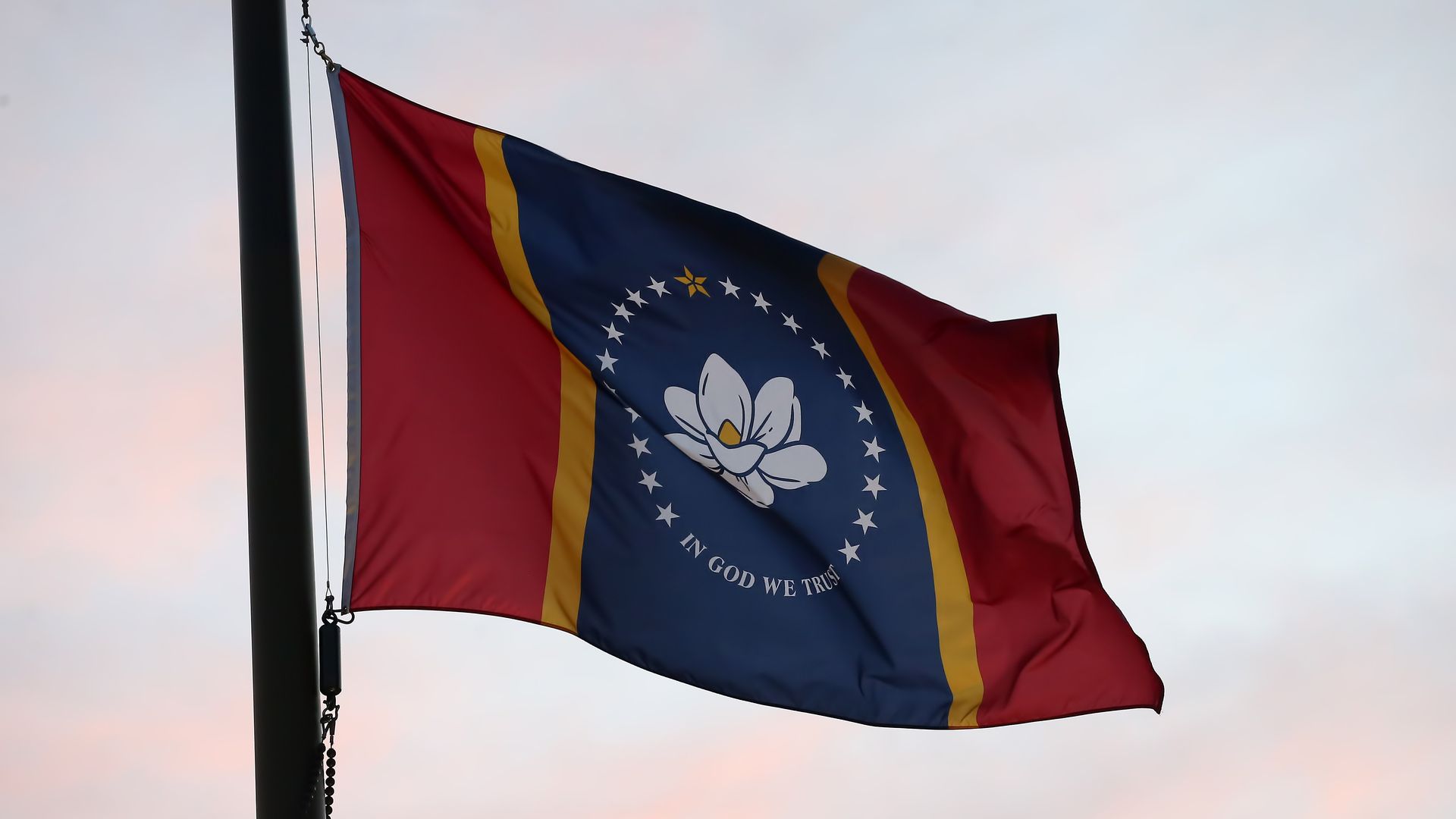 Photo of the Mississippi state flag flying from a pole as the sun sets