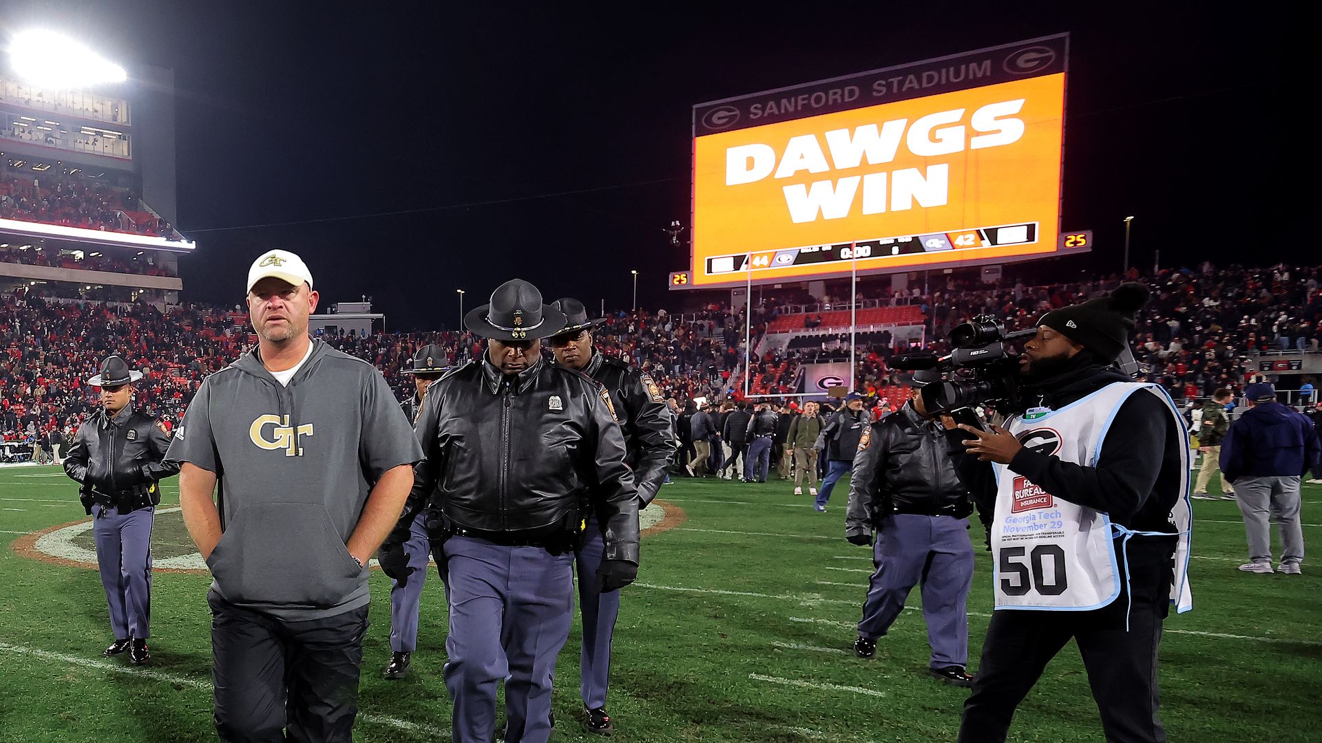 A man walks off a field in a gray hoodie and looks forlorn