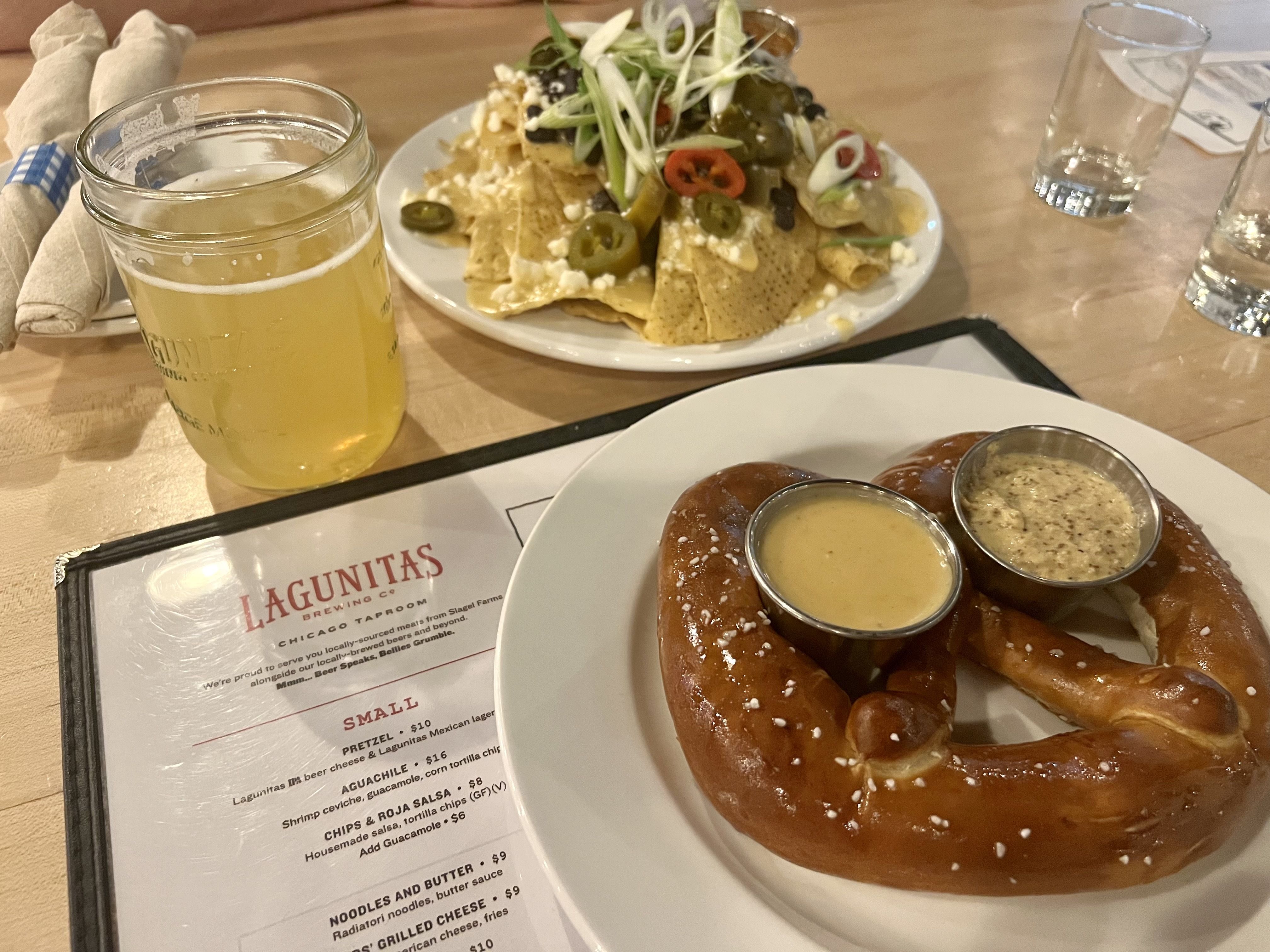 Photo of a beer, pretzel and nachos on a table. 