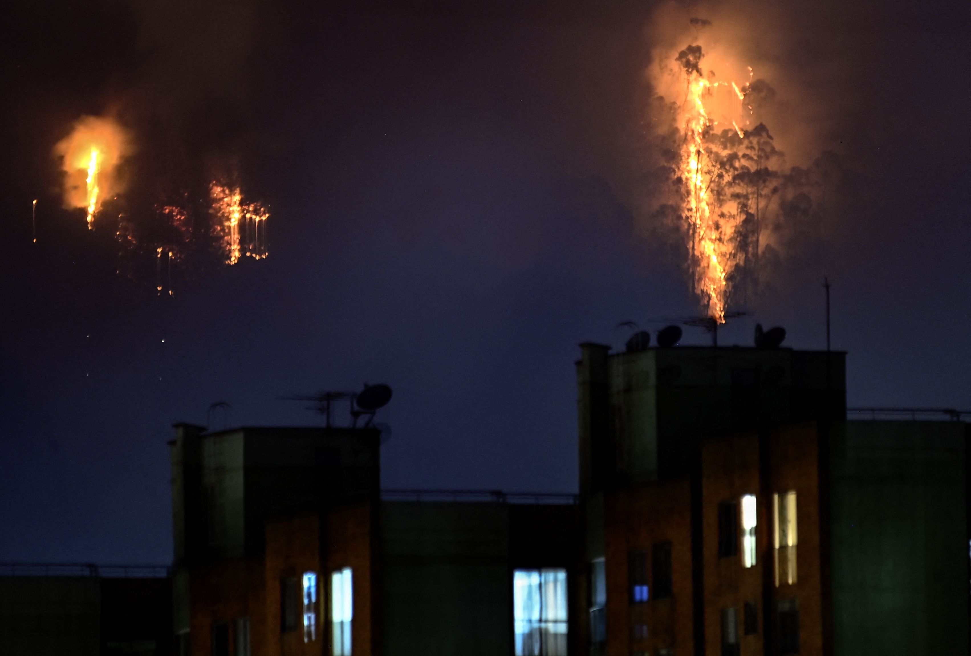 Flames are seen in the background of a photograph with apartment buildings in the foreground. 