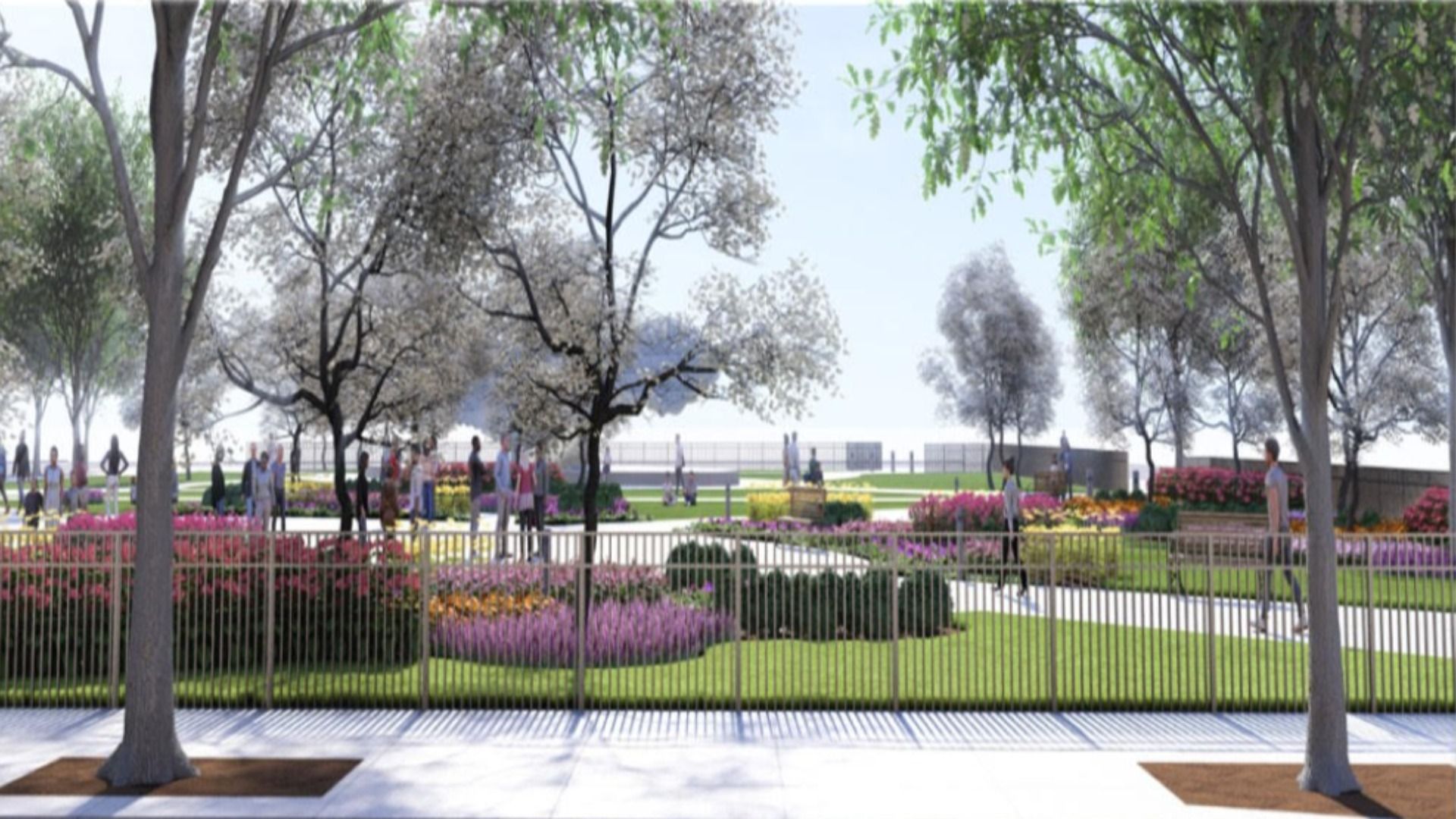 Park scene with flowering trees, a variety of colorful flower beds, green grass, paved pathways, metal fence in front, and people walking and sitting on benches under clear sky.