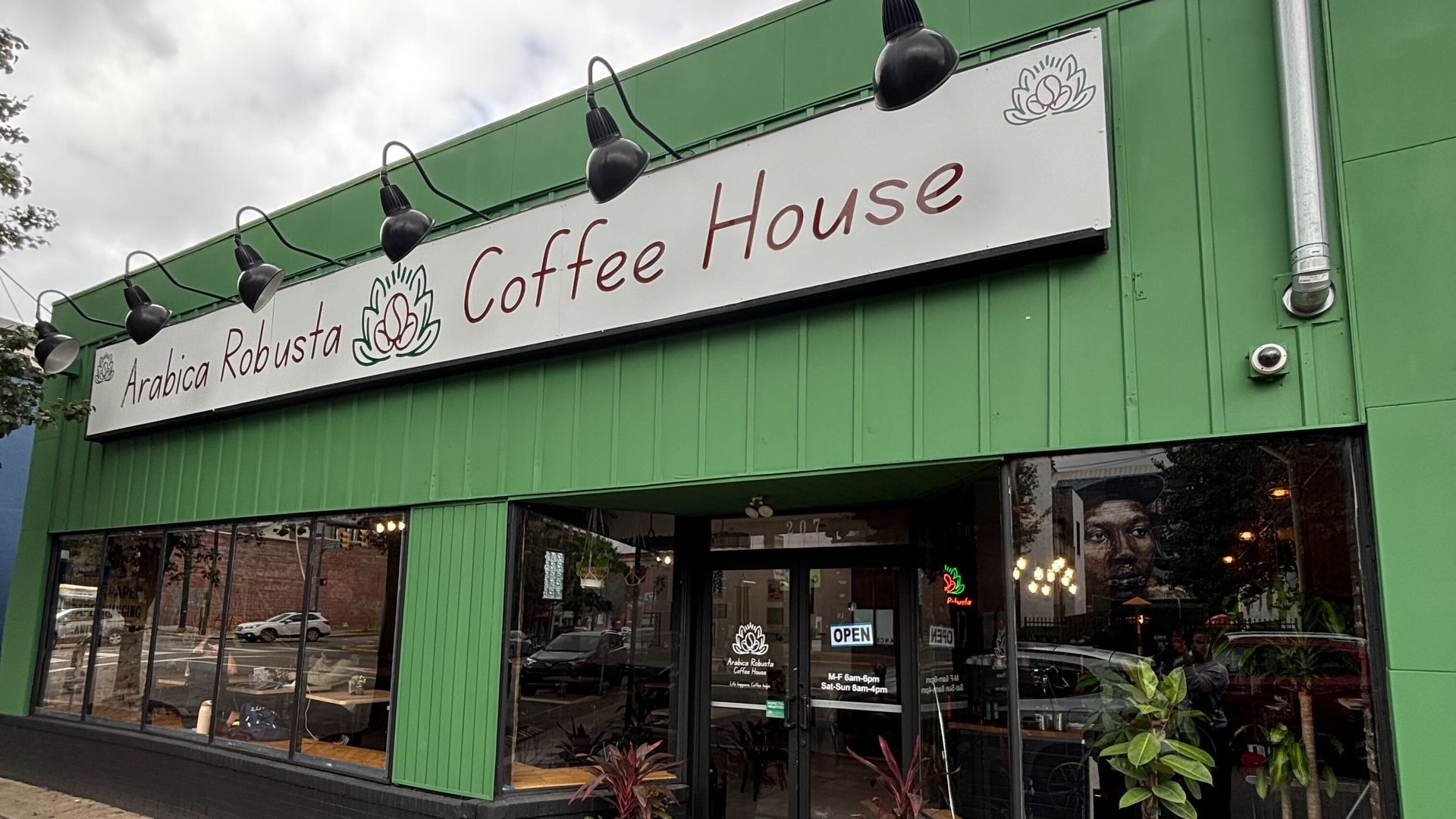 Exterior of Arabica Robusta Coffee House with green walls, large windows, and a white sign with maroon text and a coffee bean logo above the entrance, showing an "OPEN" sign on the door.