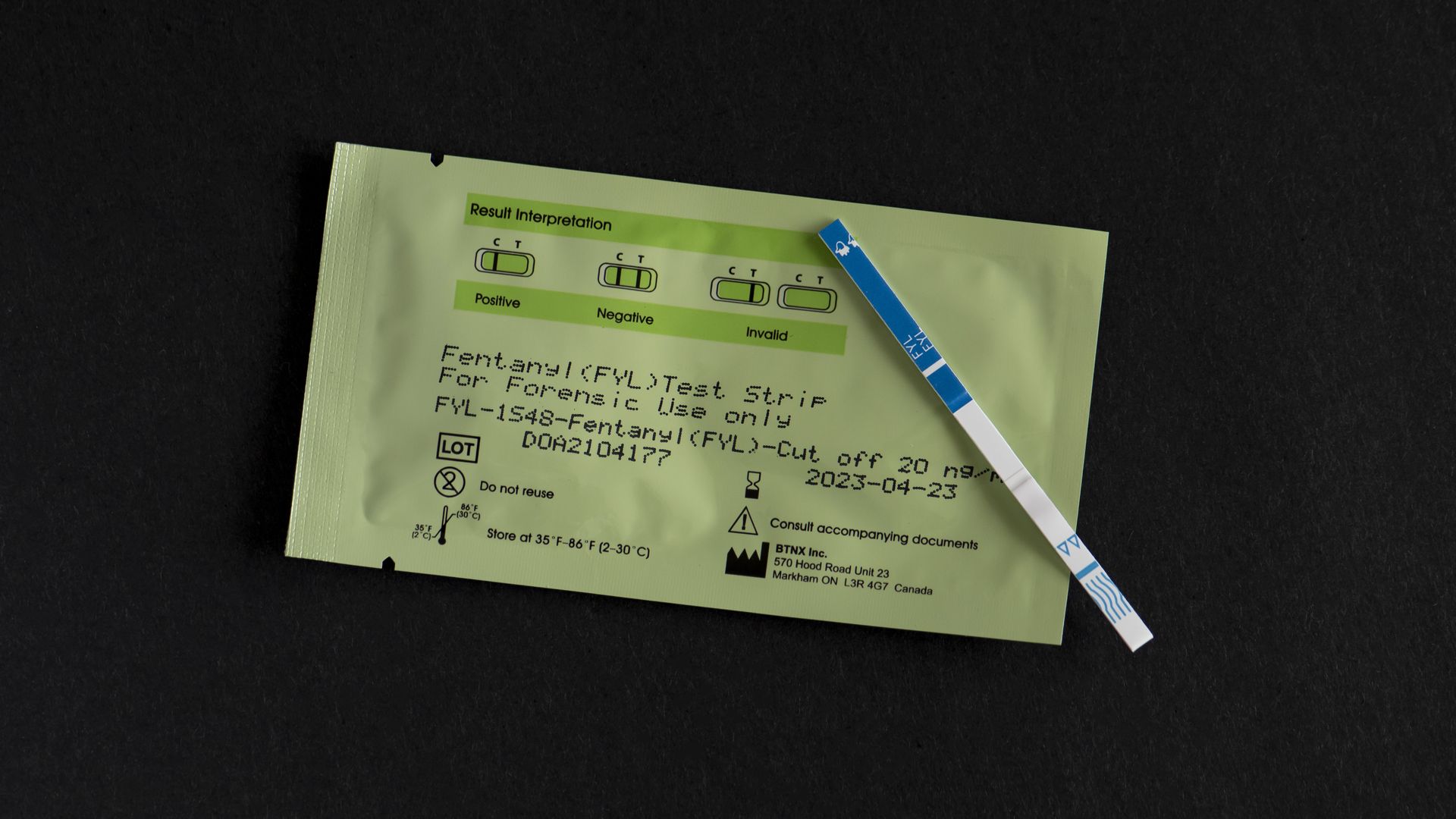 a fentanyl test strips sits on top of a package for the test strip, with a black background