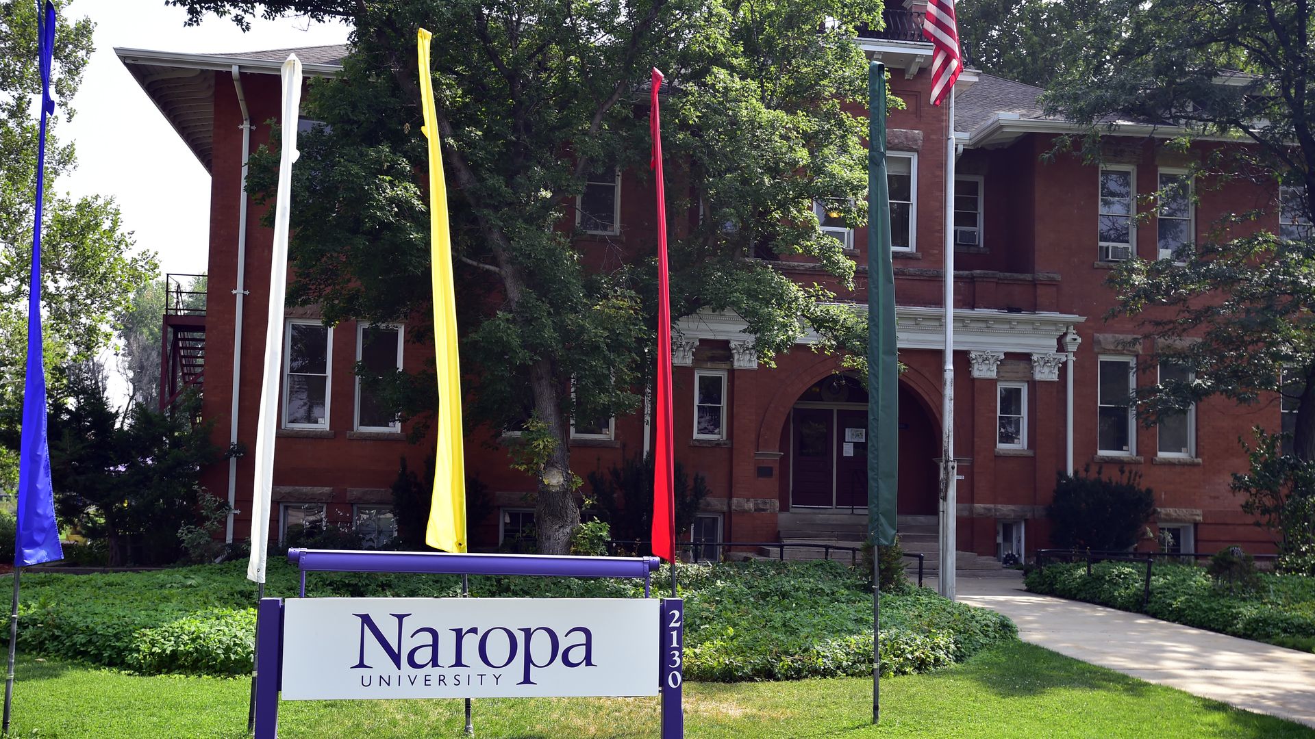 A sign with the words NAROPA UNIVERSITY outside a large, brick building with several windows in the background. 