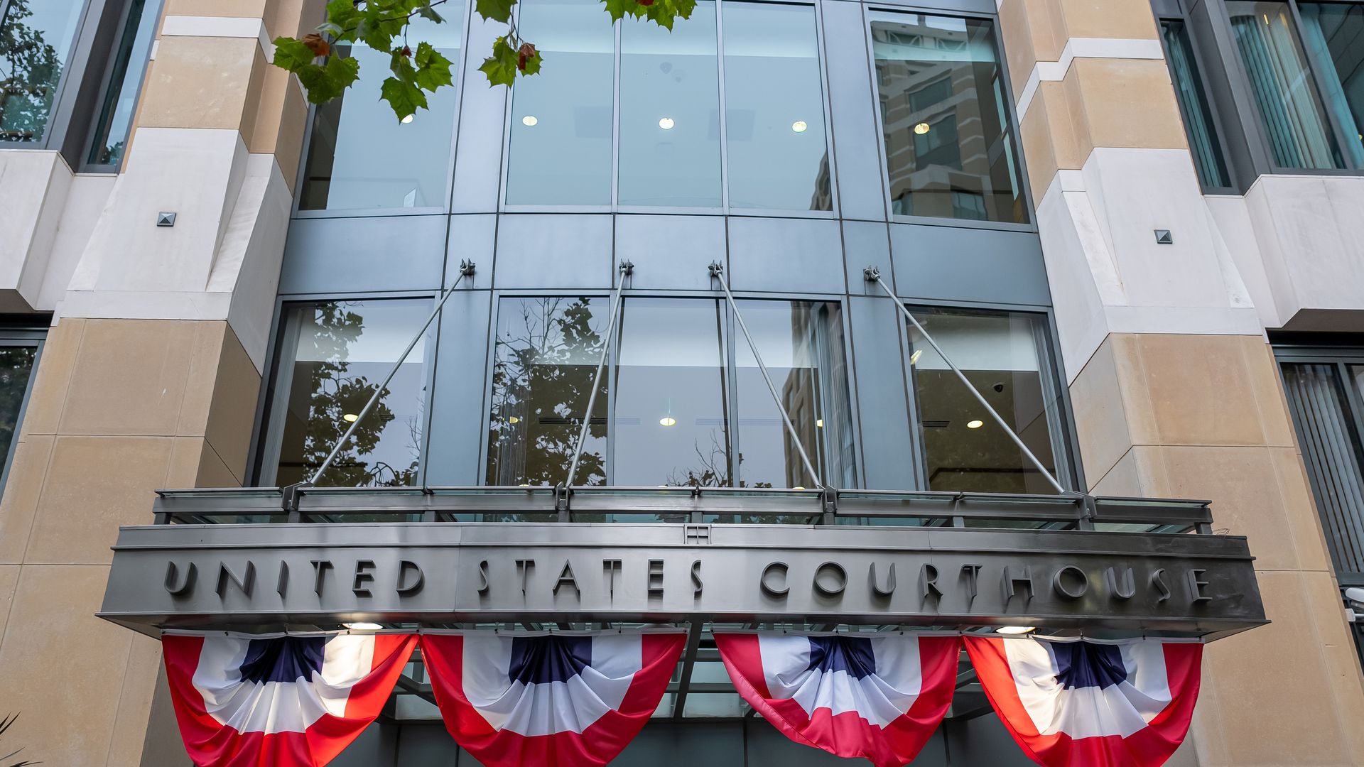 Front of a United States Courthouse with tall glass windows, beige stone façade, and red, white, and blue bunting draped above the entrance.