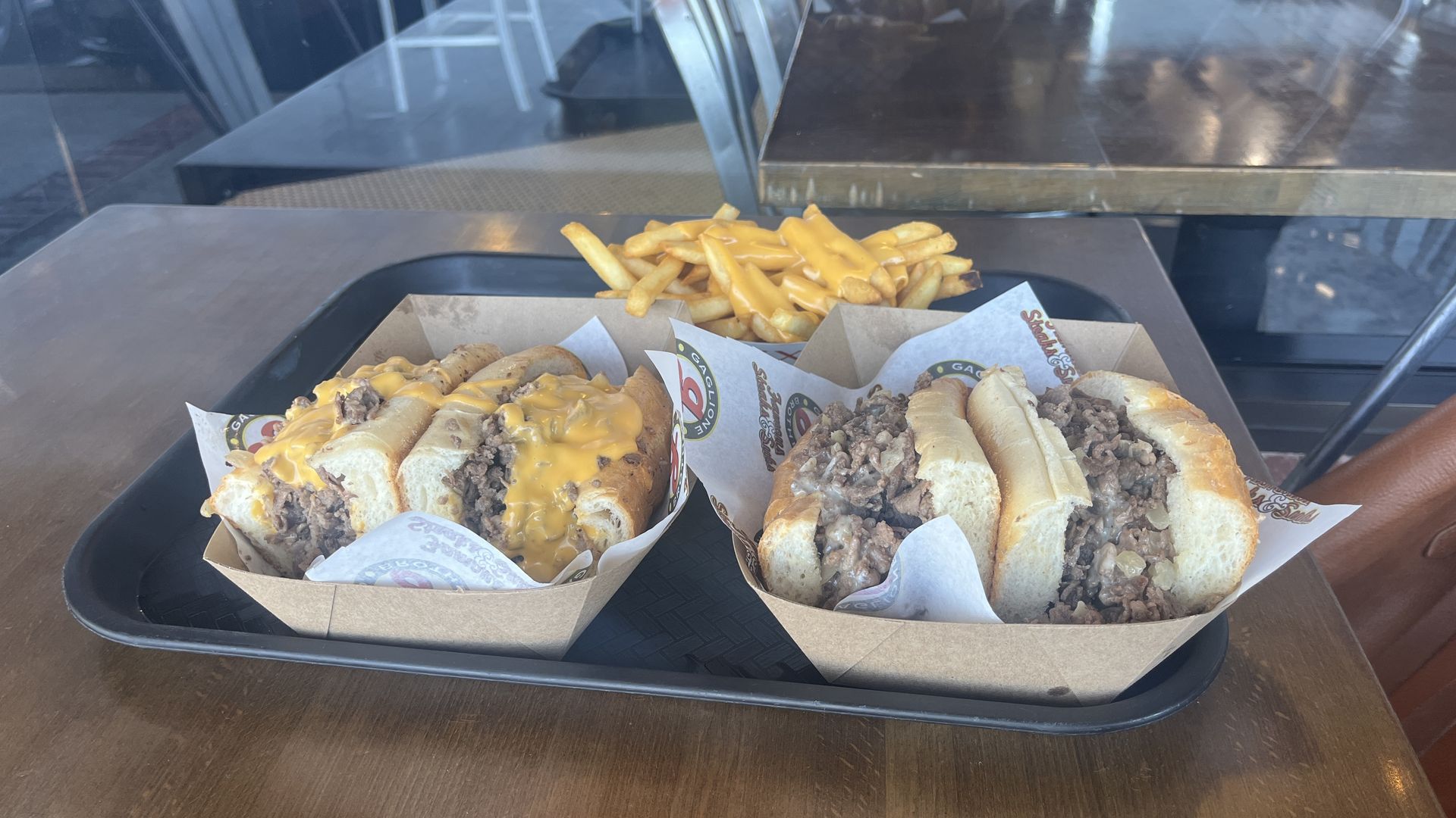 Two cheesesteaks on a tray with cheese fries.