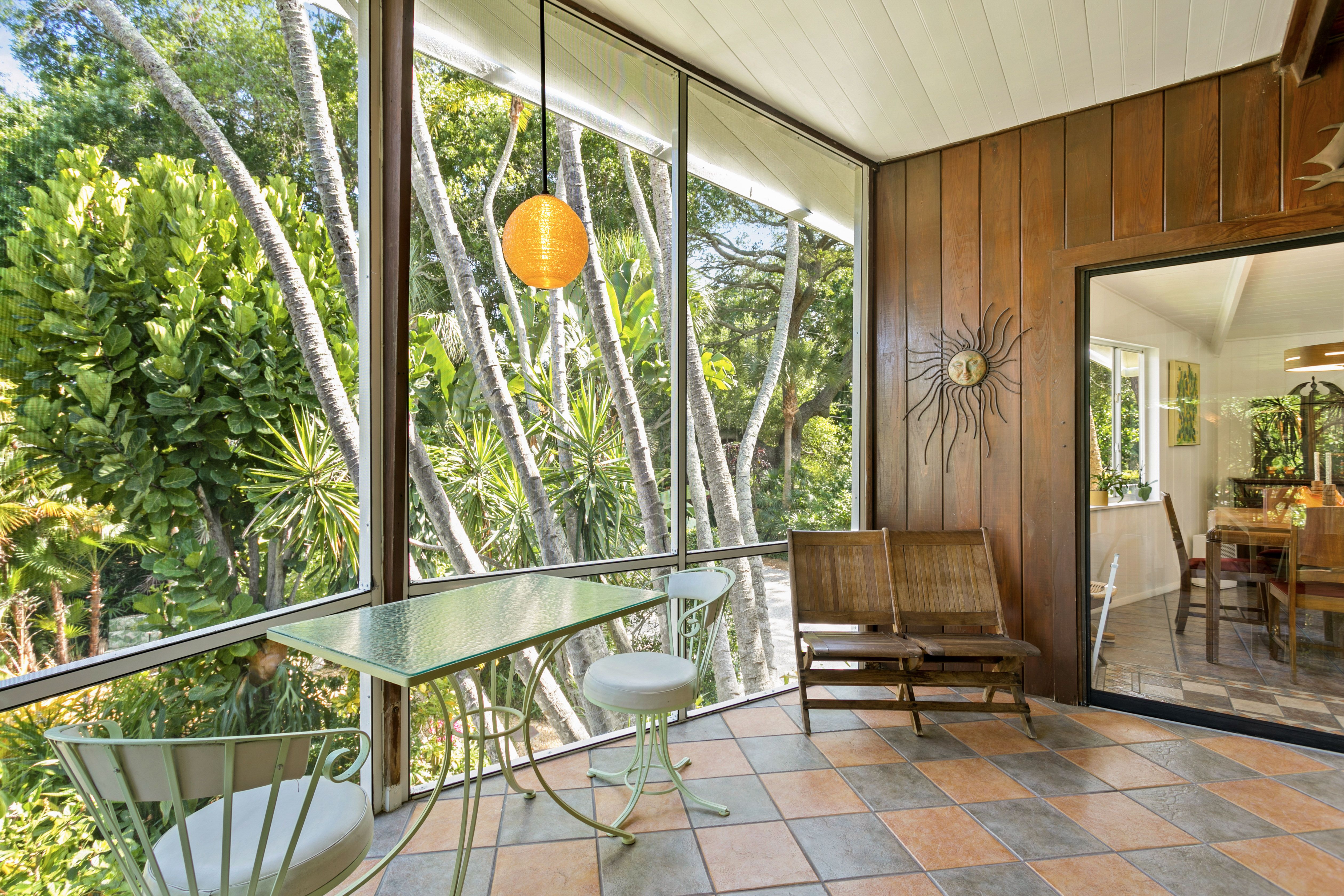 A screen porch with a table and a few chairs looking out over lush greenery. 