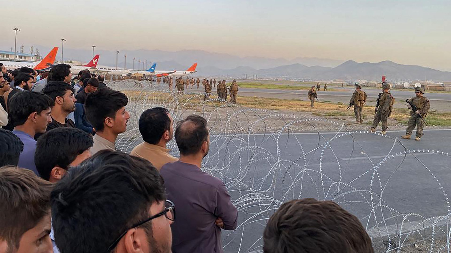Afghans watch as U.S. soldiers stand guard at Kabul's Hamid Karzai International Airport on Monday.