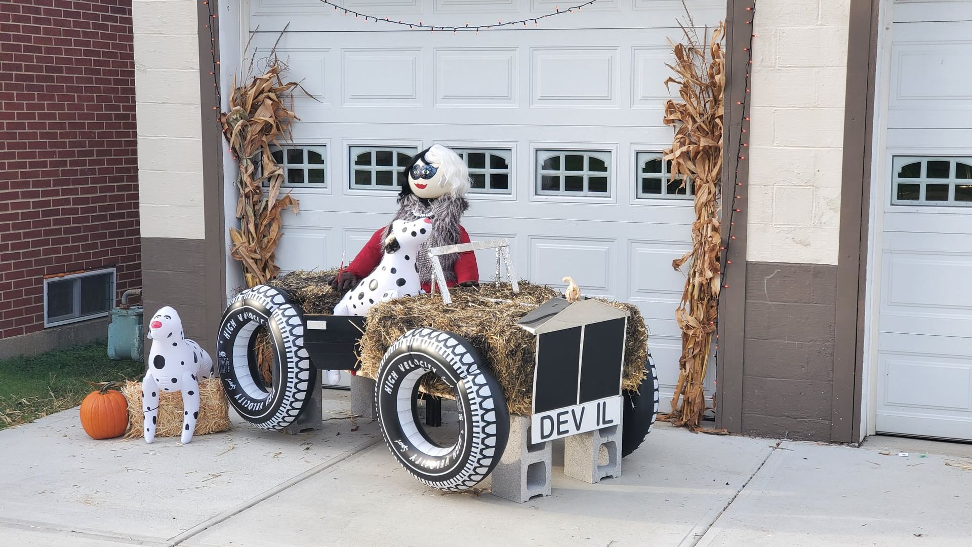A 101 Dalmatians themed scarecrow display with Cruella Devil sitting in a car next to a blow up dalmatian. 