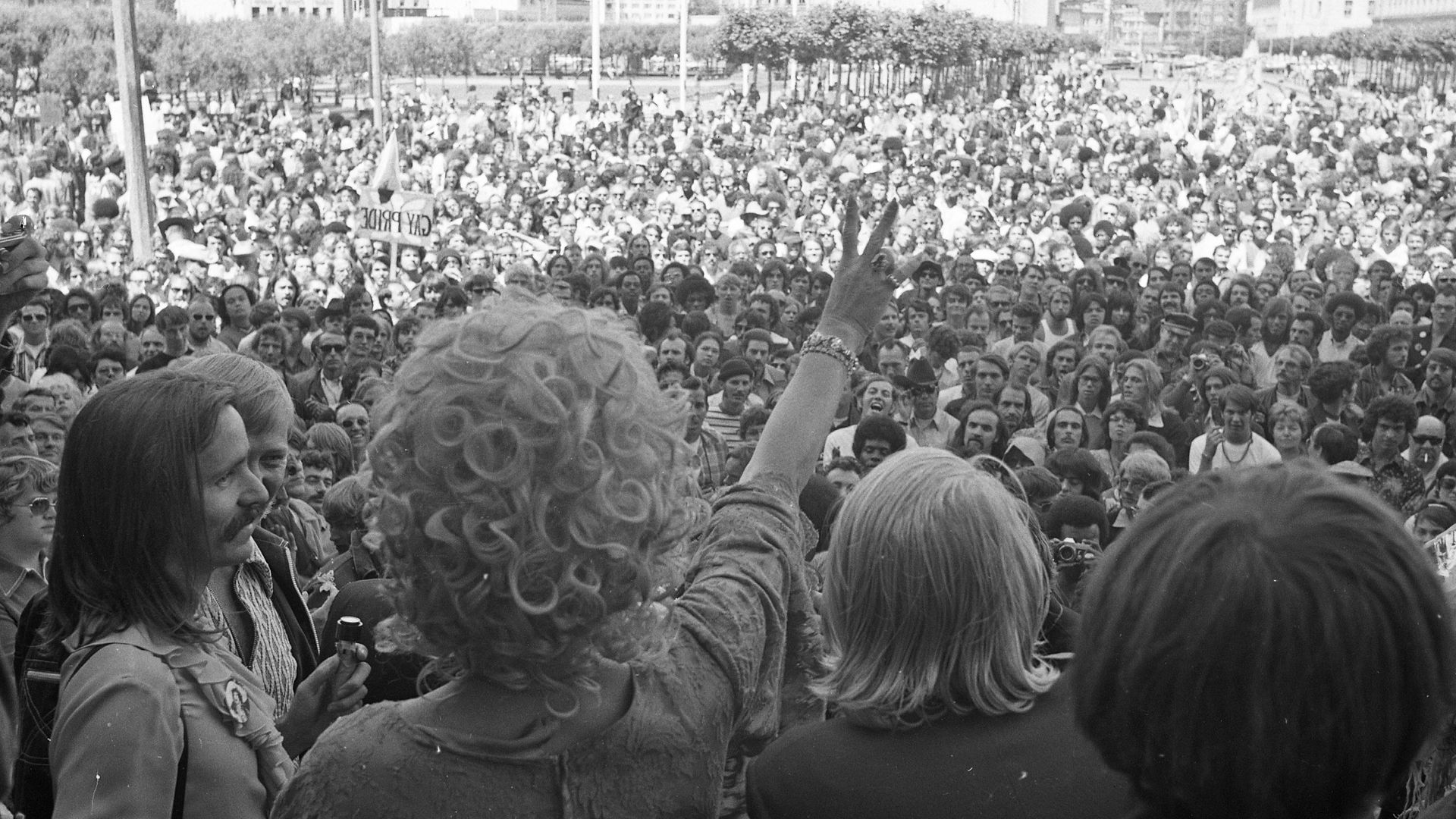Photo of crowds assembled before a stage where one person is raising a V sign with their hand