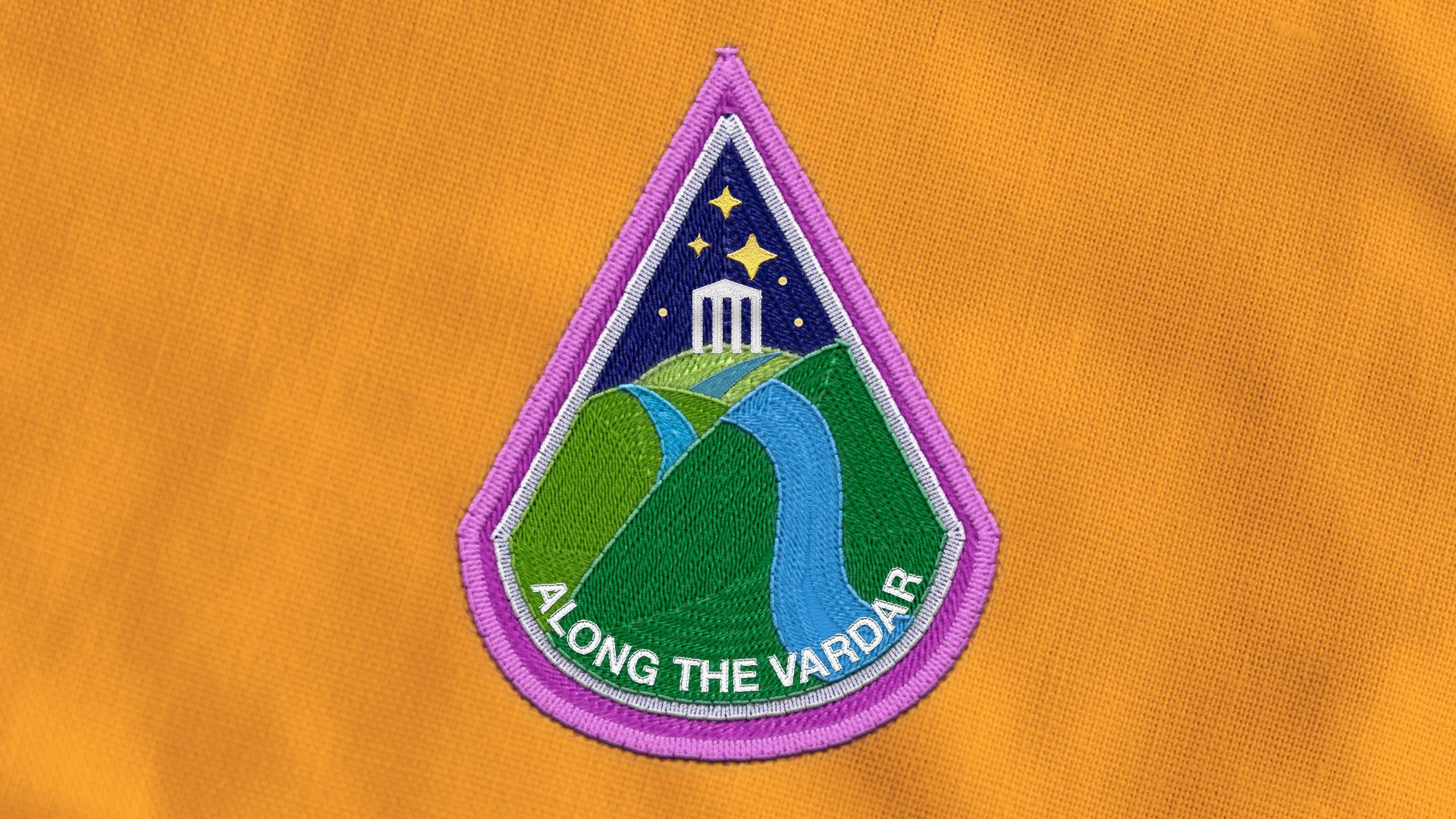 Illustration of an astronaut badge depicting a river over rolling hills with a Grecian temple in the background, the words "ALONG THE VARDAR" are on the badge. 