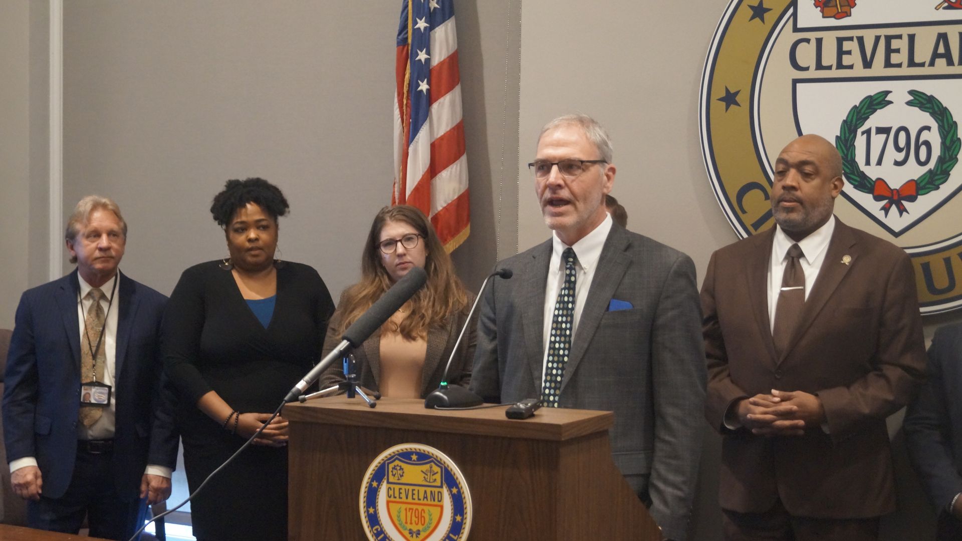 Members of Cleveland City Council at a press conference at city hall. A gray-suited Kris Harsh speaks at a lectern.