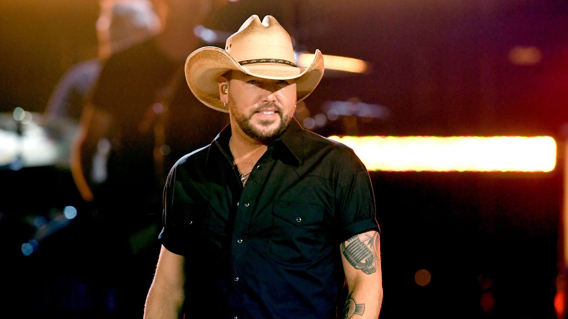 Country singer Jason Aldean stands on stage in a cowboy hat and black shirt. 