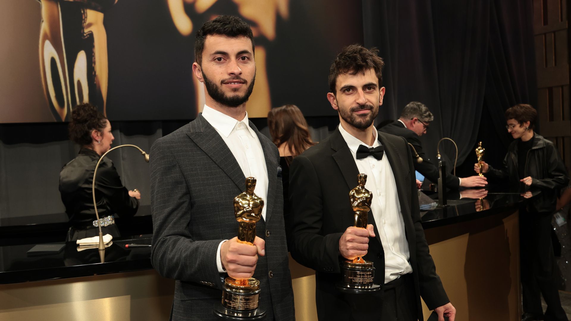 Two filmmakers stand with their Oscar awards. 