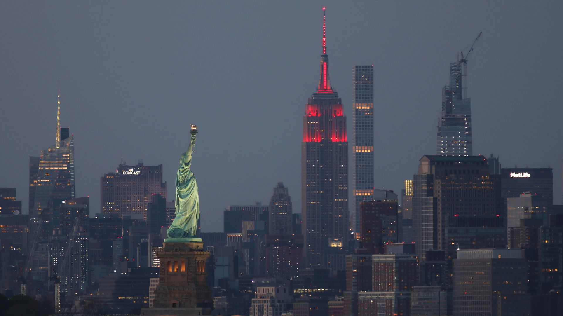 : Th Empire State Building sits behind the Statue of Liberty in New York City as it continues to honor COVID-19 healthcare workers by being lit in red on May 3, 2020 in Bayonne, New Jersey