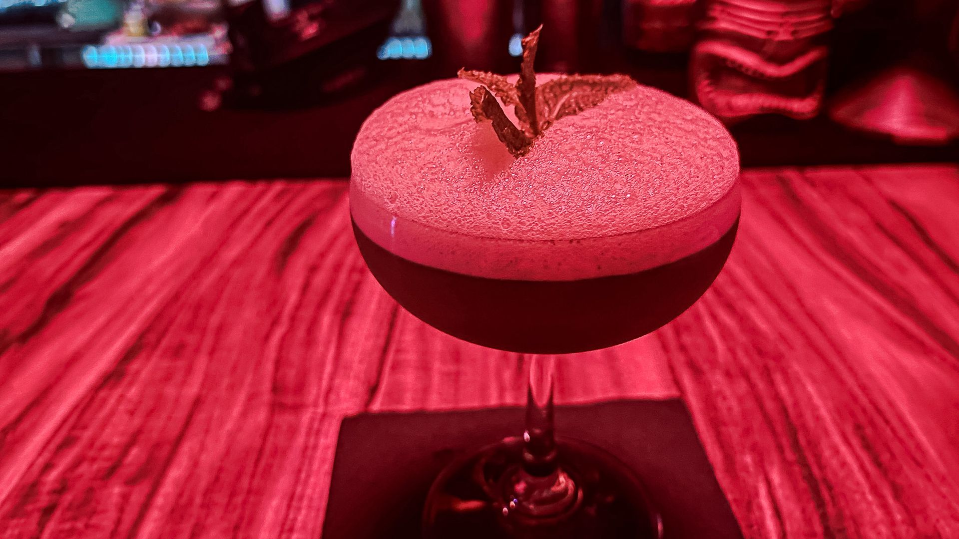 A pink-glow bar has a foamy cocktail with mint on top.