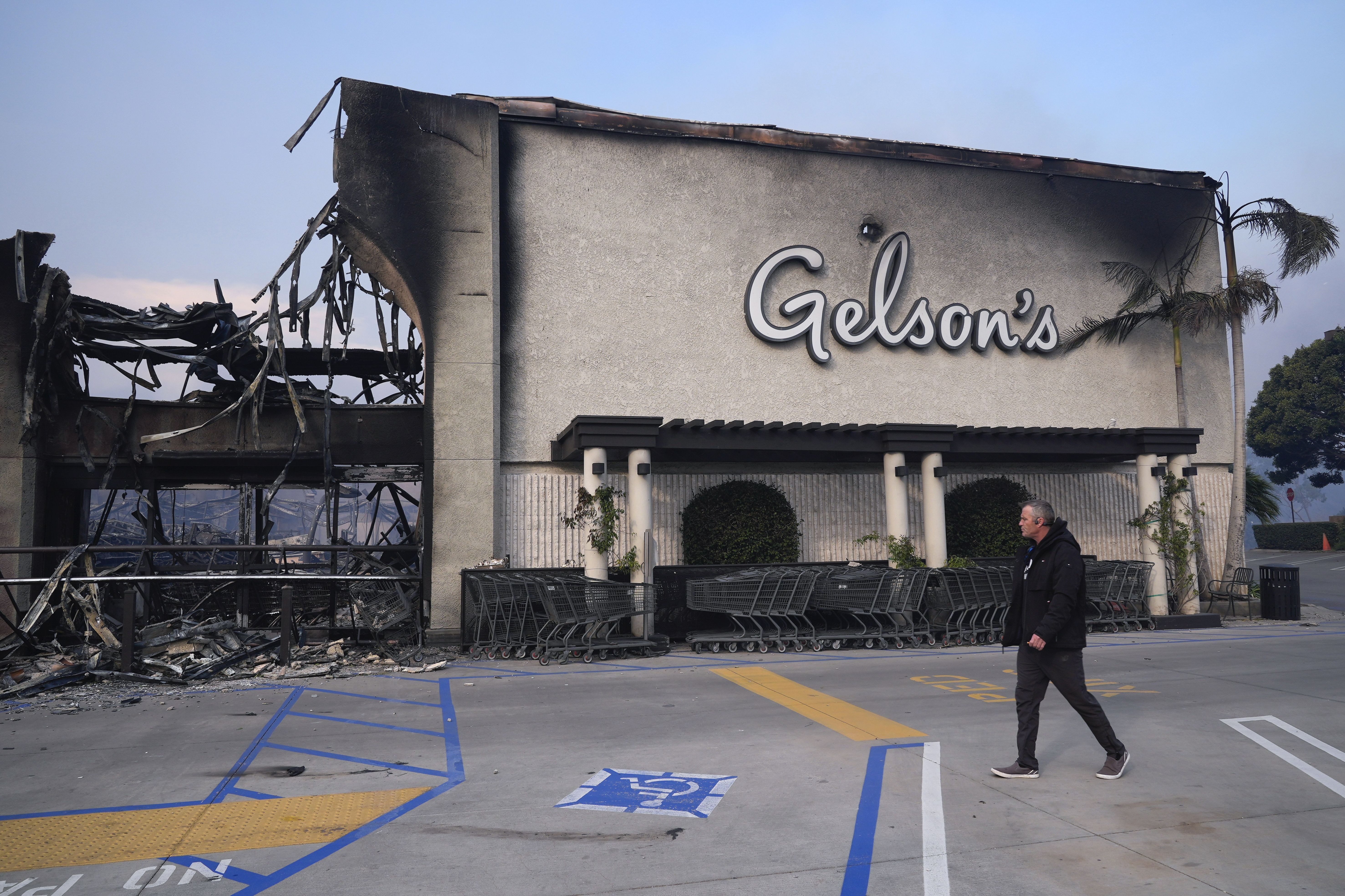 A man walks by Gelson's as the Palisades Fire ravages a neighborhood amid high winds in the Pacific Palisades neighborhood of Los Angeles, Wednesday, Jan. 8, 2025. (AP Photo/Damian Dovarganes)