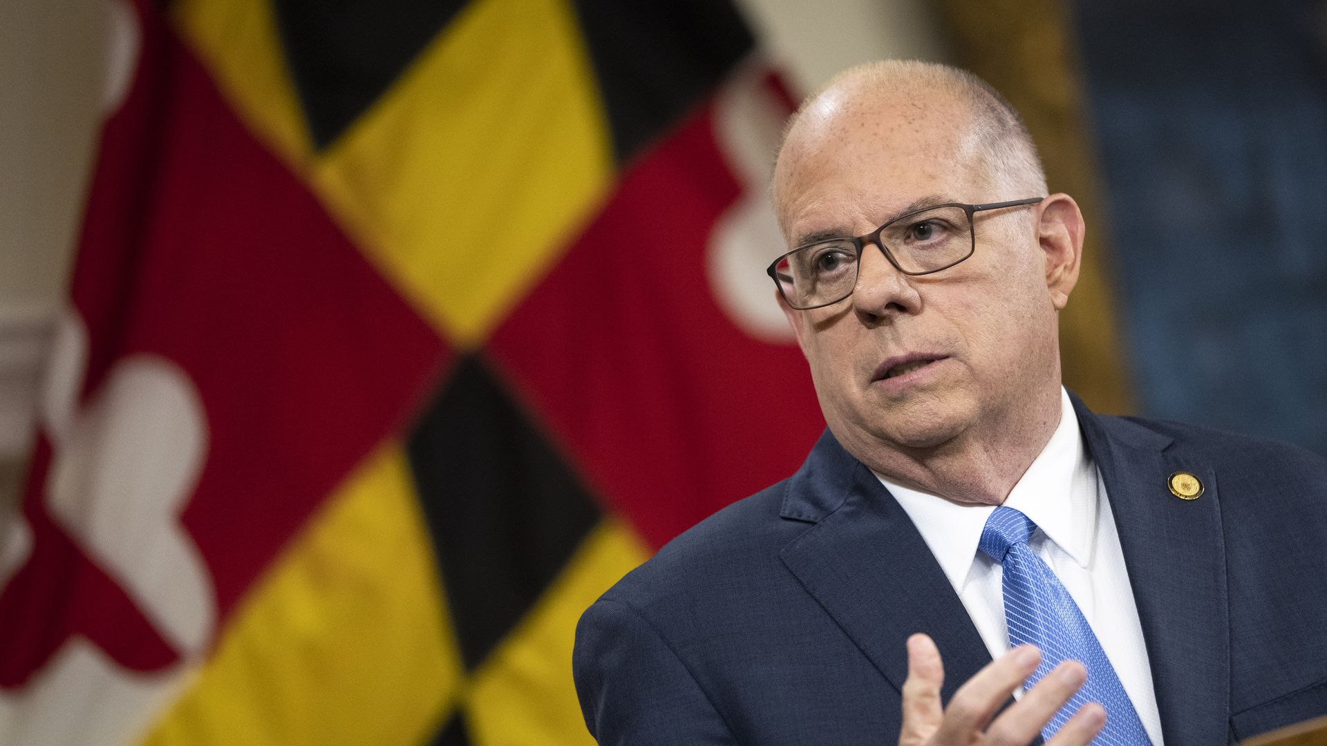 Maryland Gov. Larry Hogan gestures with his right hand at a lectern with the Maryland flag behind him
