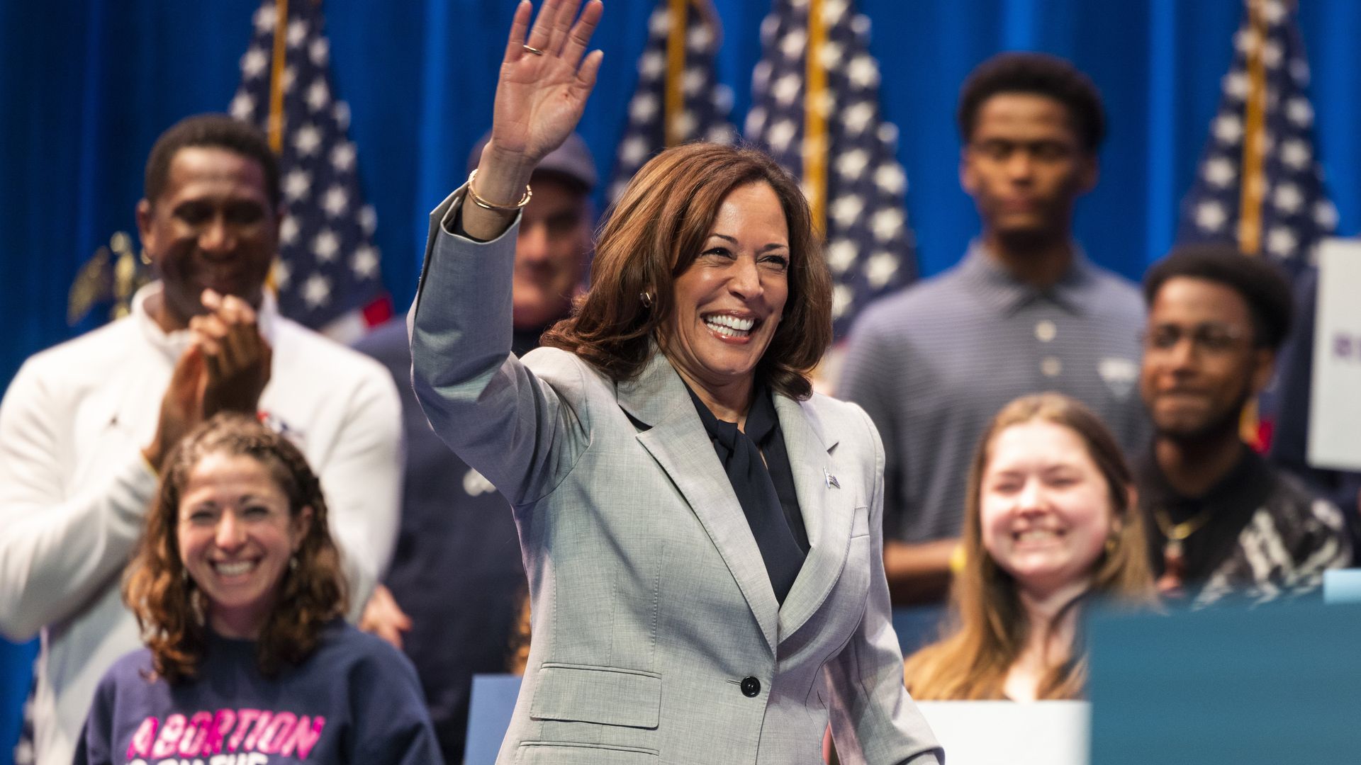 Kamala Harris in a grey suit waving in front of students at Howard University