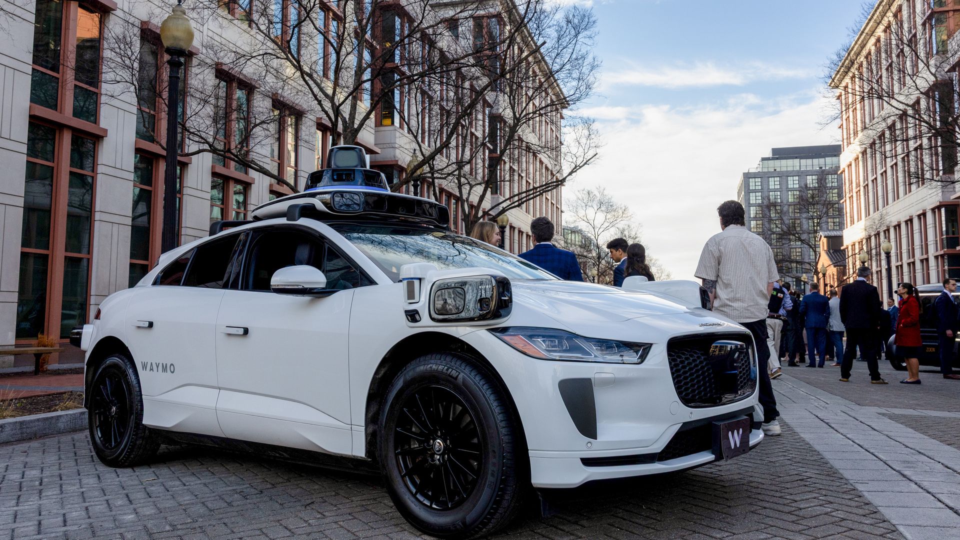 A white Jaguar SUV Waymo vehicle is parked on a D.C. street outside the Department of Transportation headquarters
