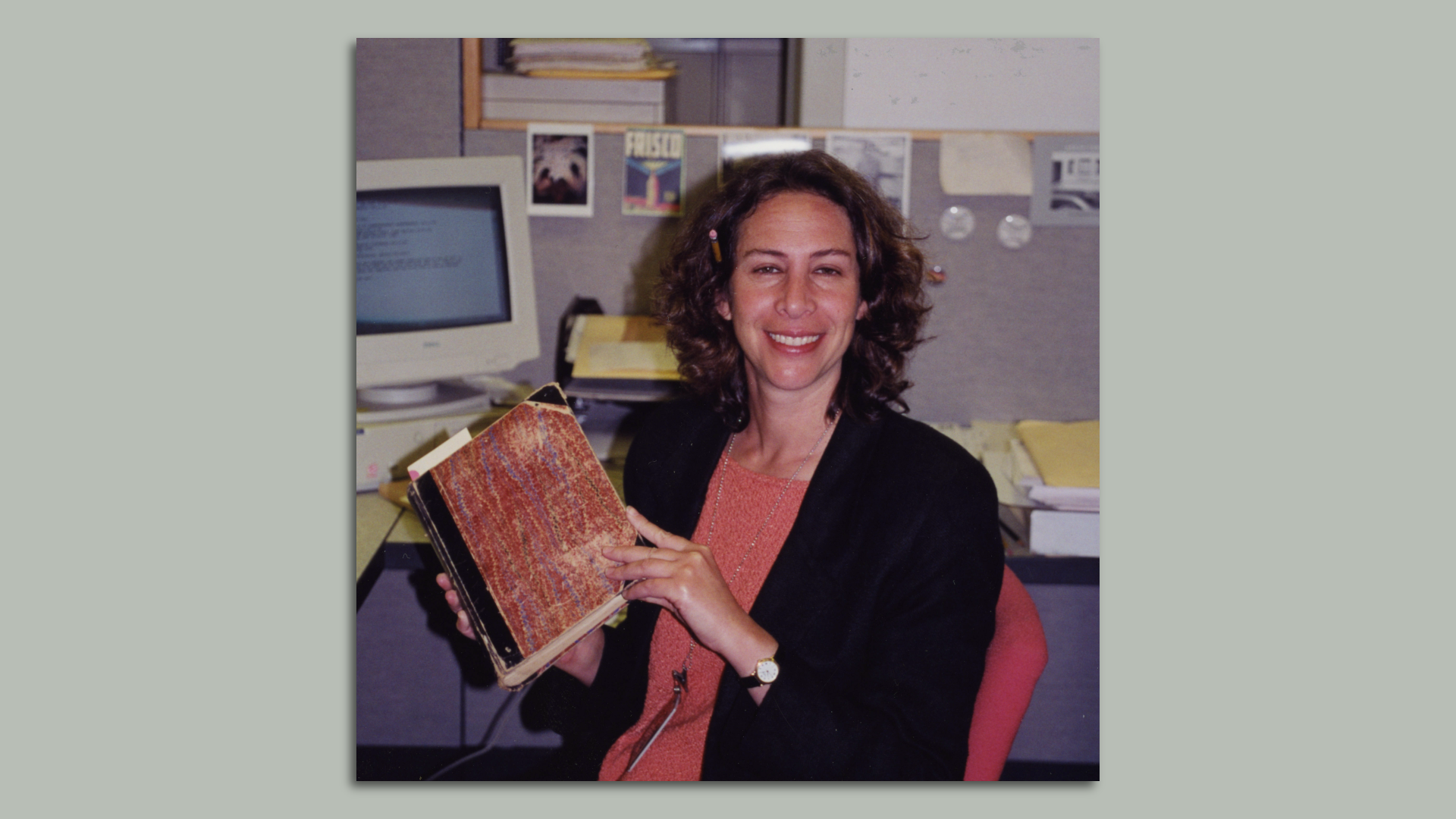 Photo of Susan Goldstein holding an archival book while she smiles at the camera