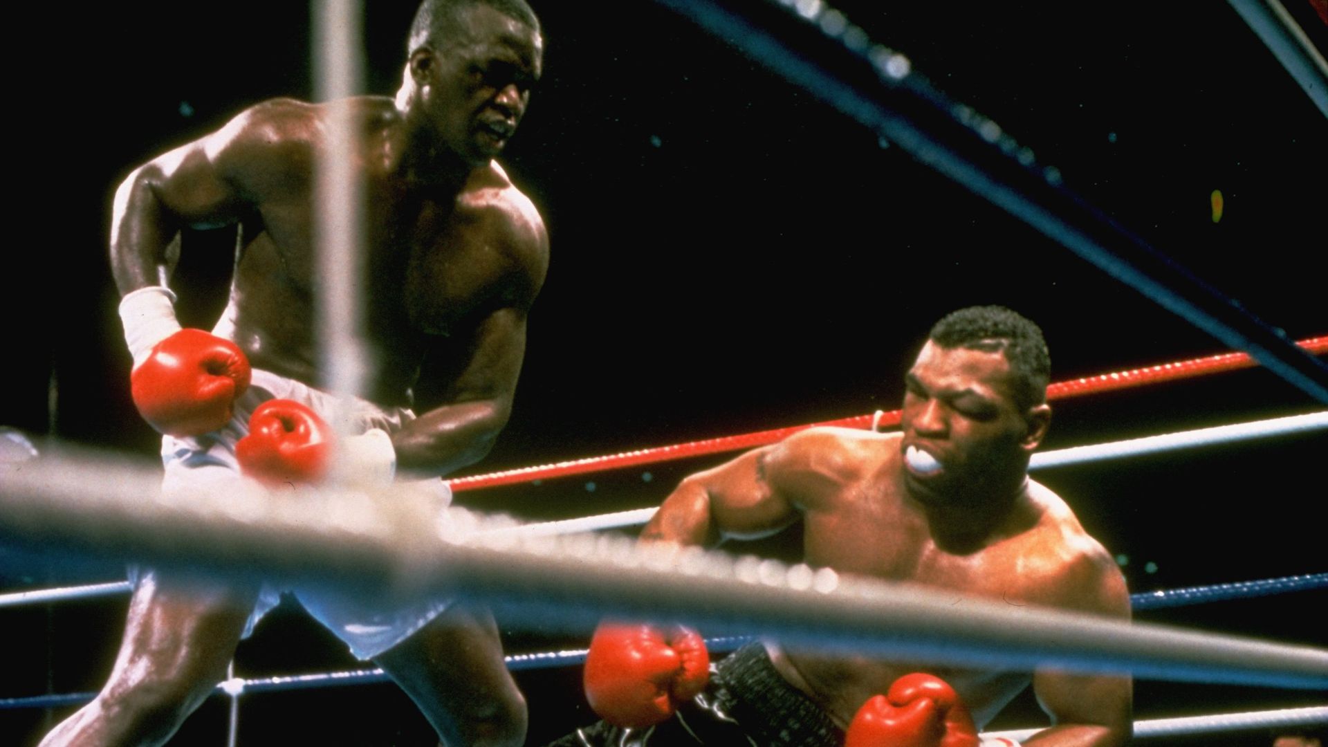 Buster Douglas stands over Mike Tyson, who is falling to the boxing mat. 