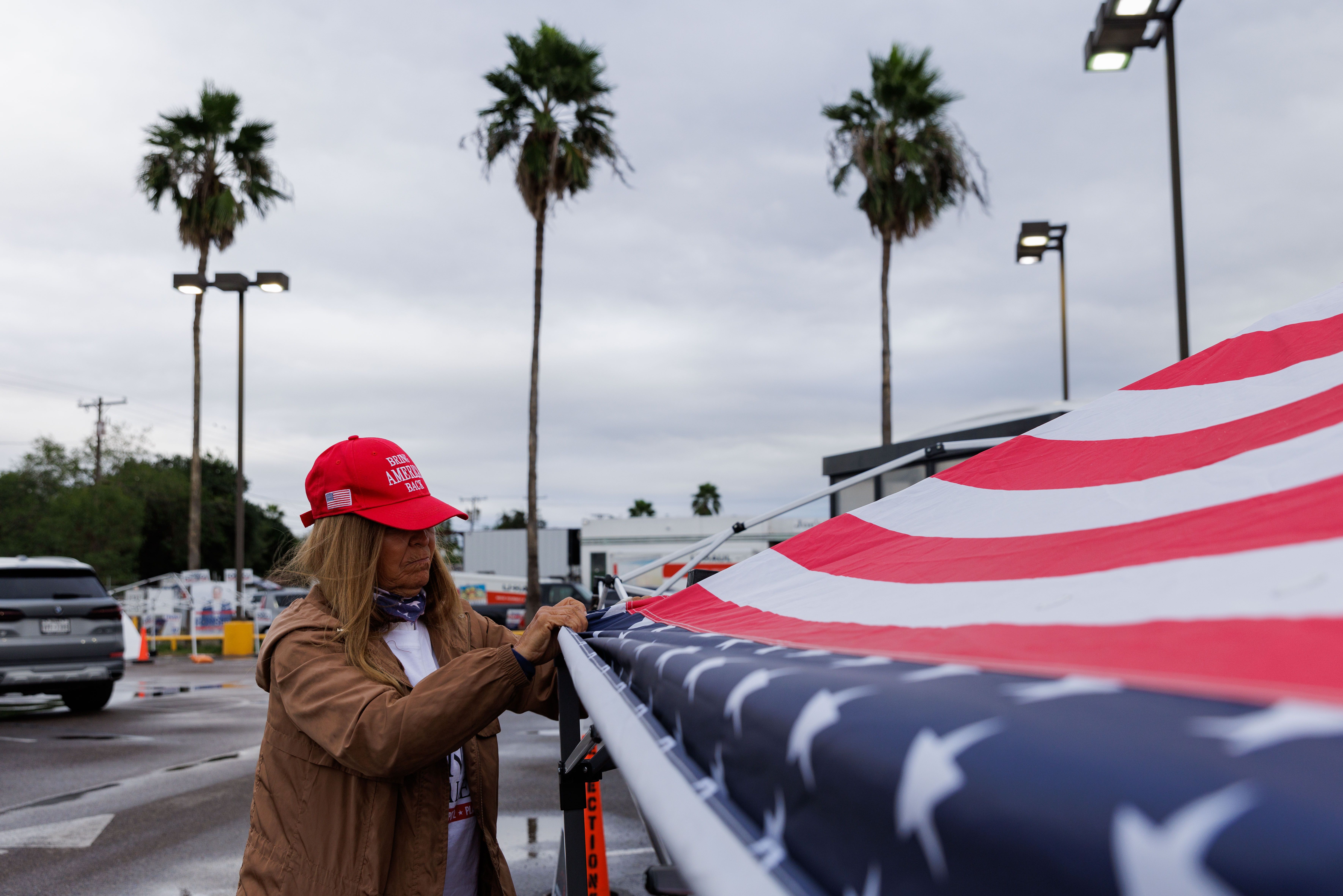 A woman wearing a MAGA hat sets up an American flag canopy to campaign for Donald Trump.  