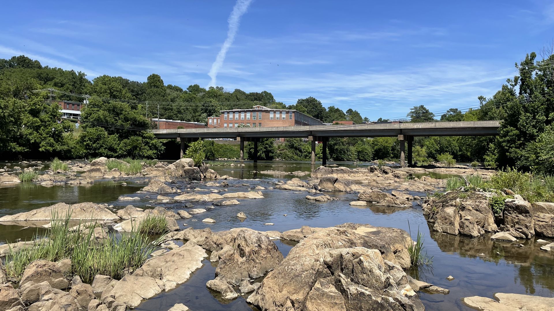 A rocky river winds under a bridge with an old mill on the left side of the river. 